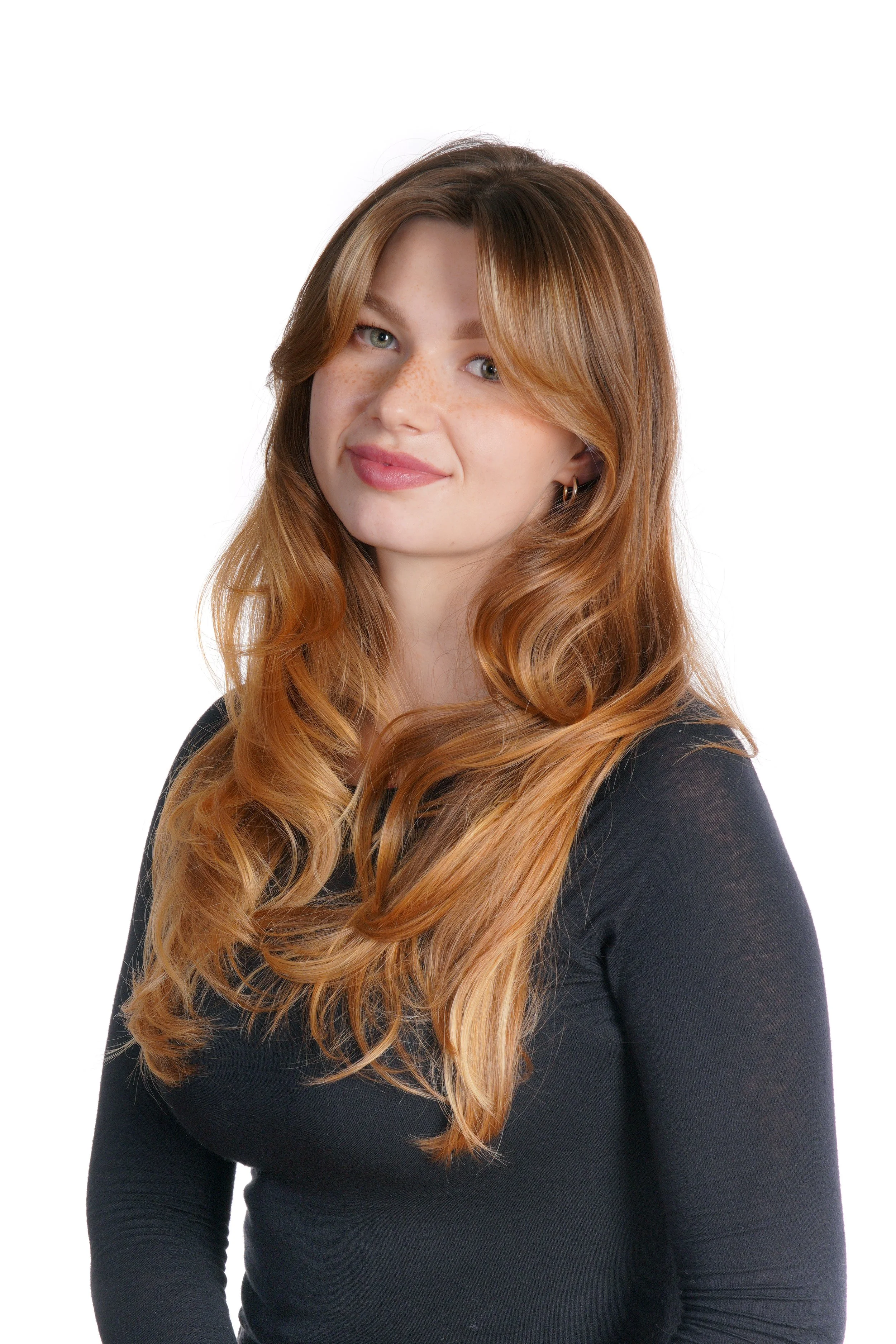 A woman with long, wavy red hair, wearing a black top, smiling softly, against a white background.