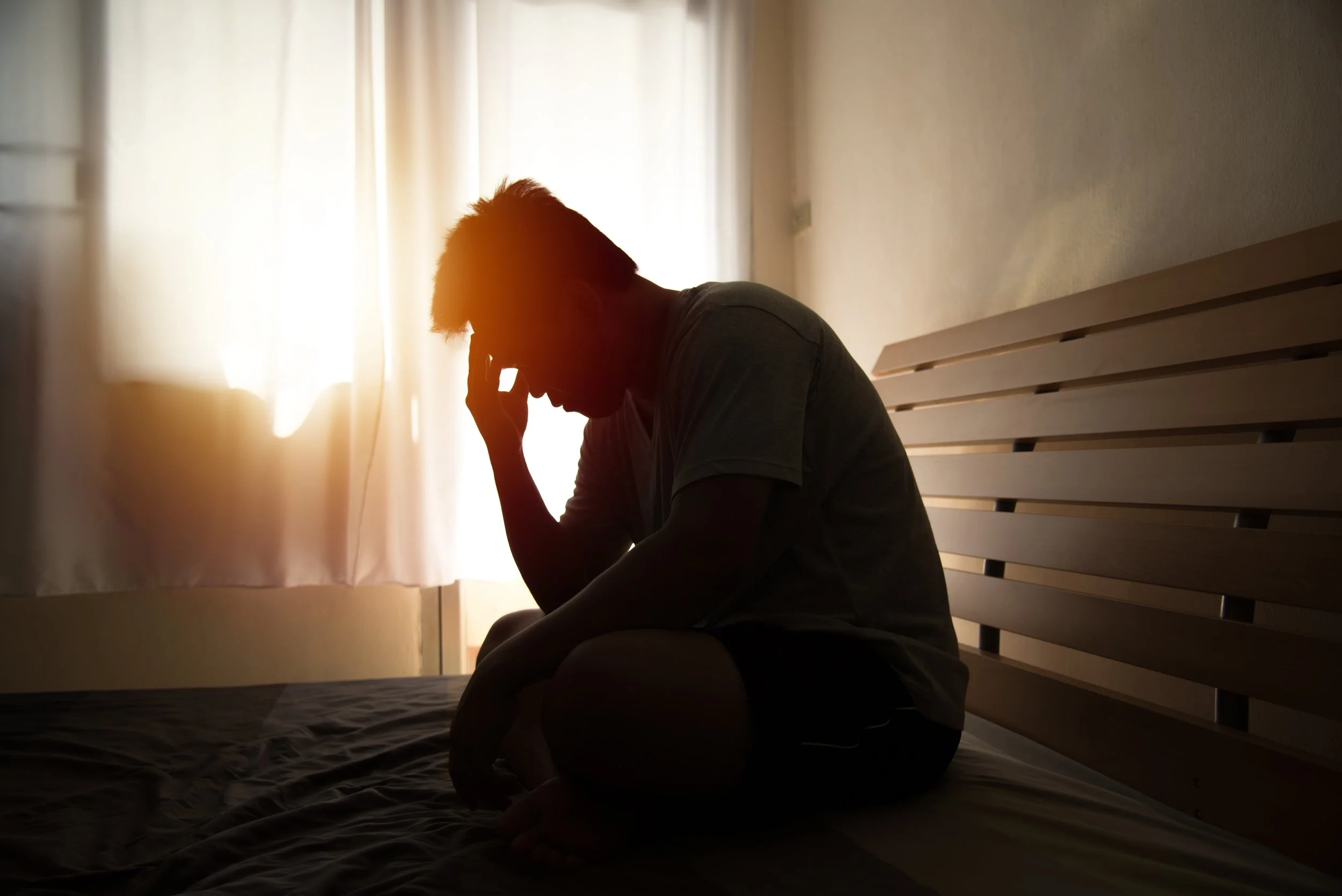 Άτομο καθισμένο σε κρεβάτι με το χέρι στο κεφάλι, ένδειξη έντονου πόνου ή δυσφορίας.