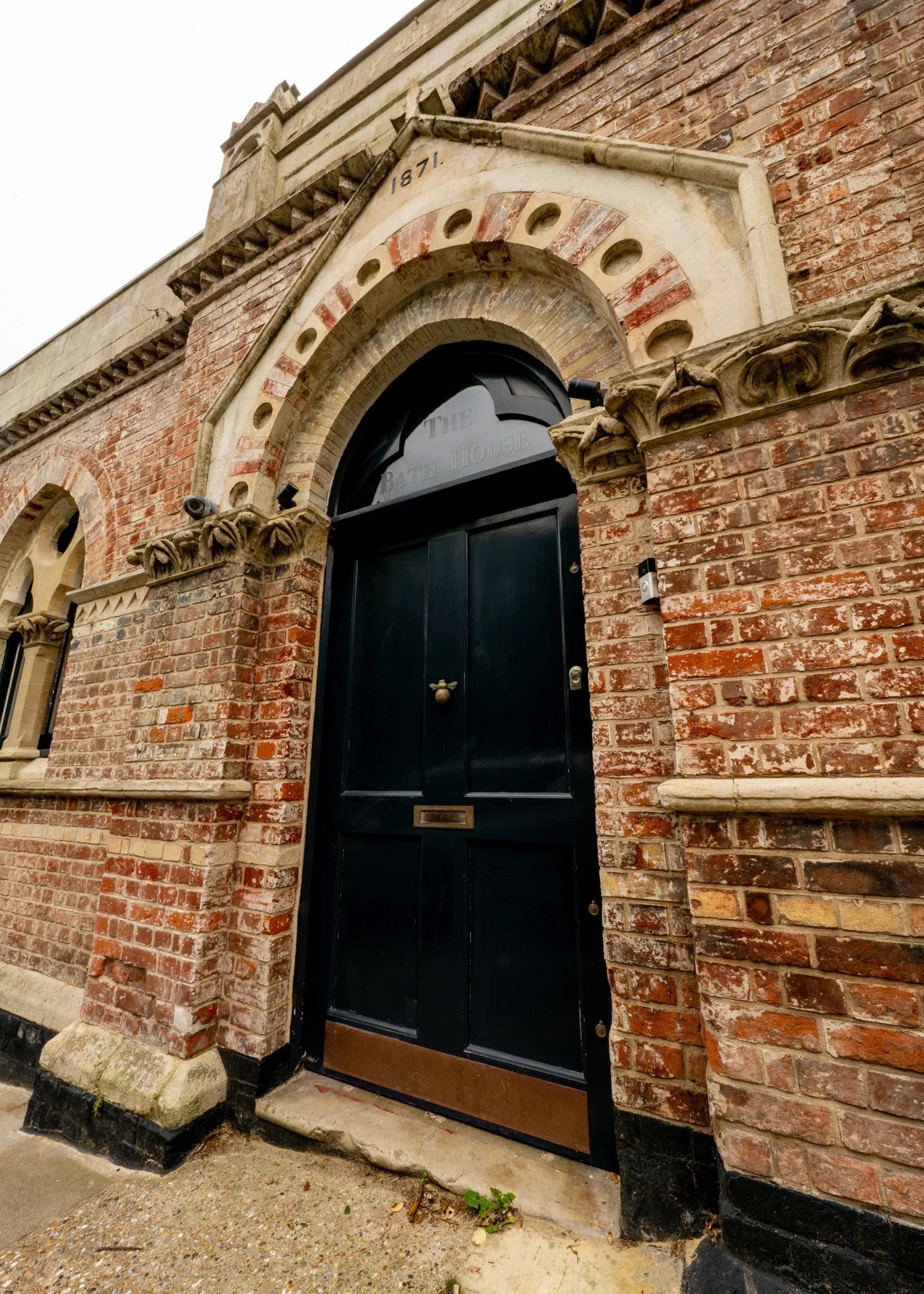 A historic brick building with an arched black door and decorative stone accents, including a date inscribed as 1871.