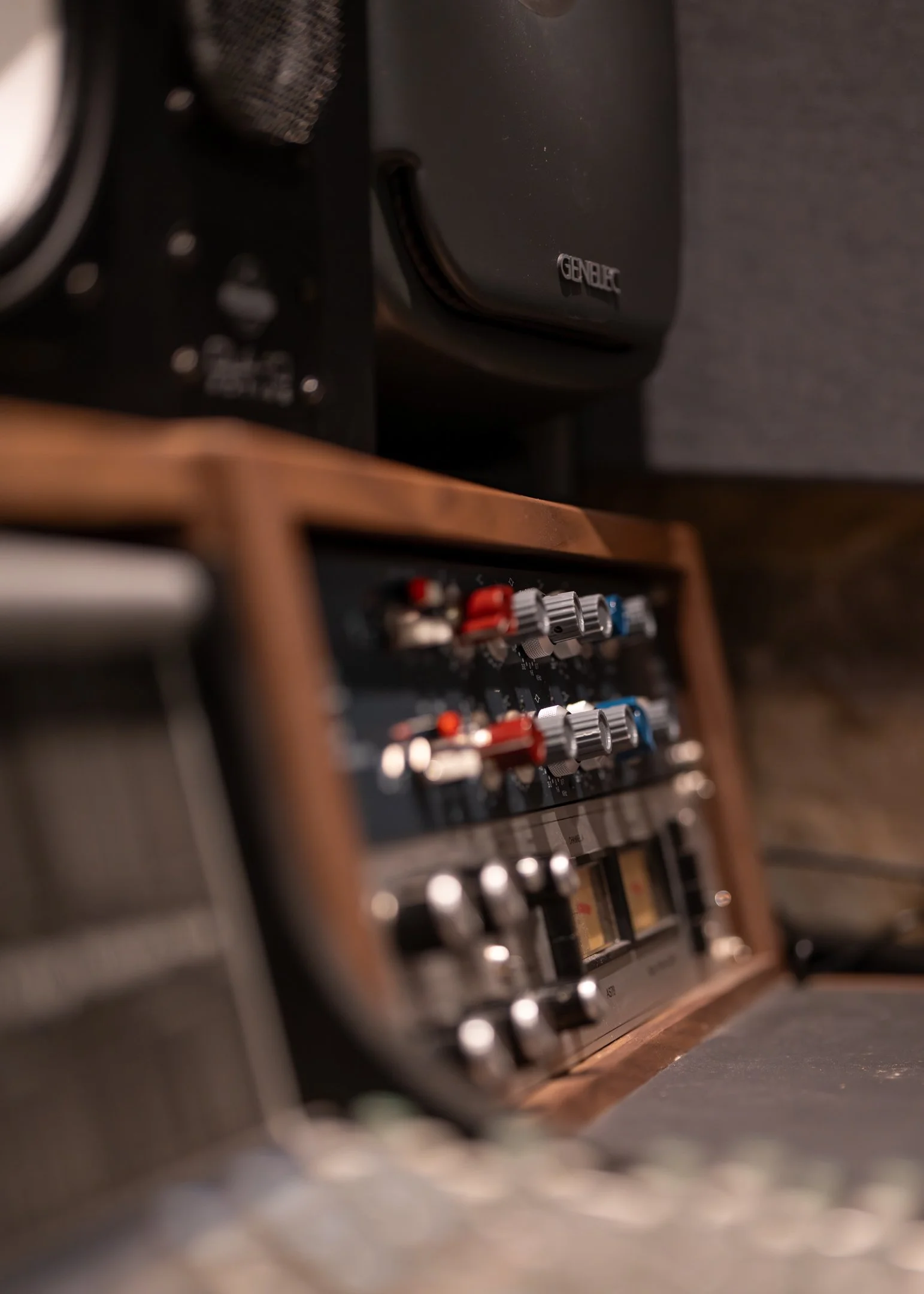 Close-up of a vintage audio equalizer with knobs and sliders, set within a wooden frame, and a speaker labeled 'Genelec' in the background.