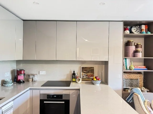 Modern kitchen with beige cabinets, a stovetop, oven, and open shelving with decorative items and dishes.