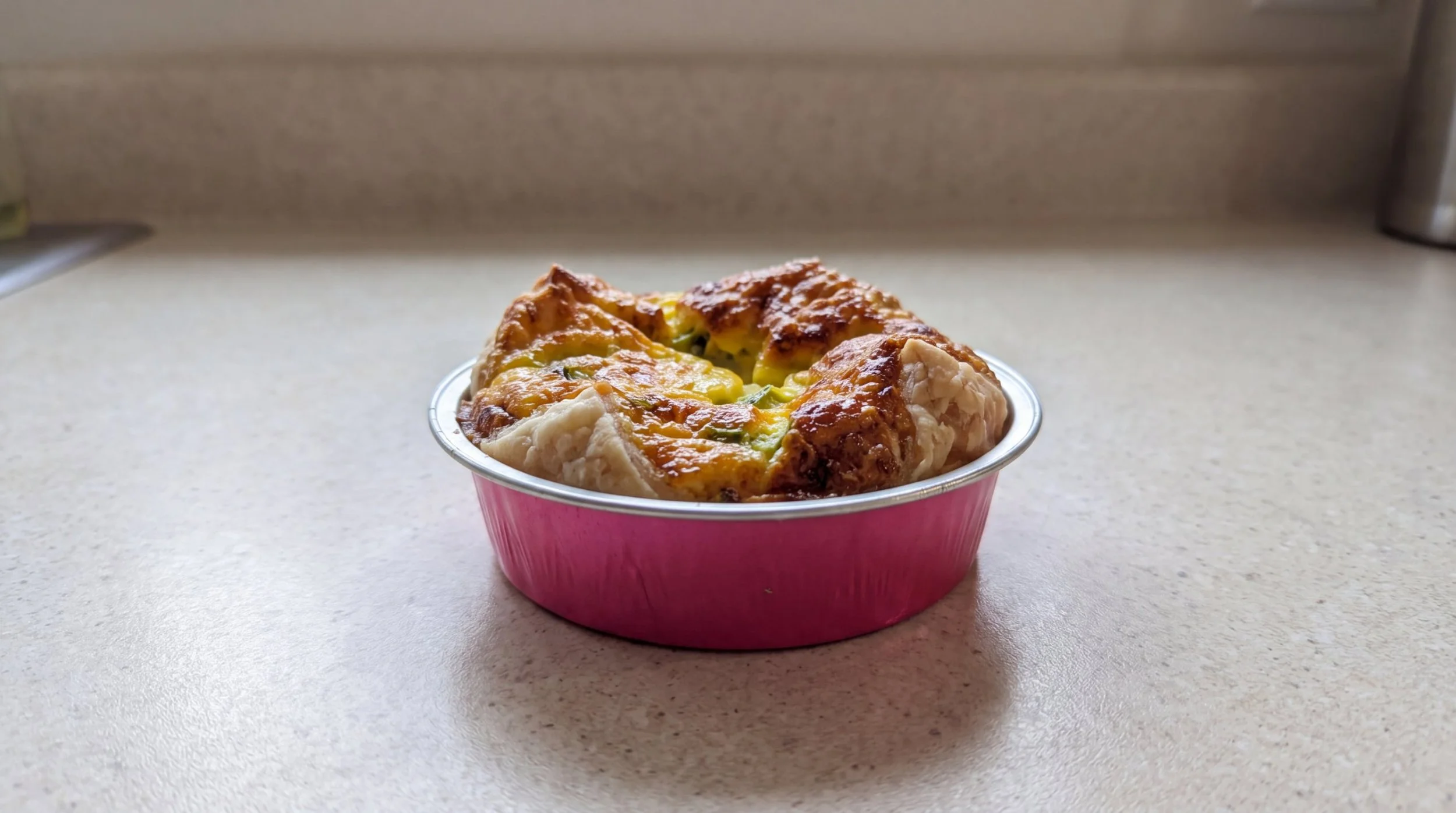 Side view of a baked Parmesan asparagus personal quiche in a pink tin