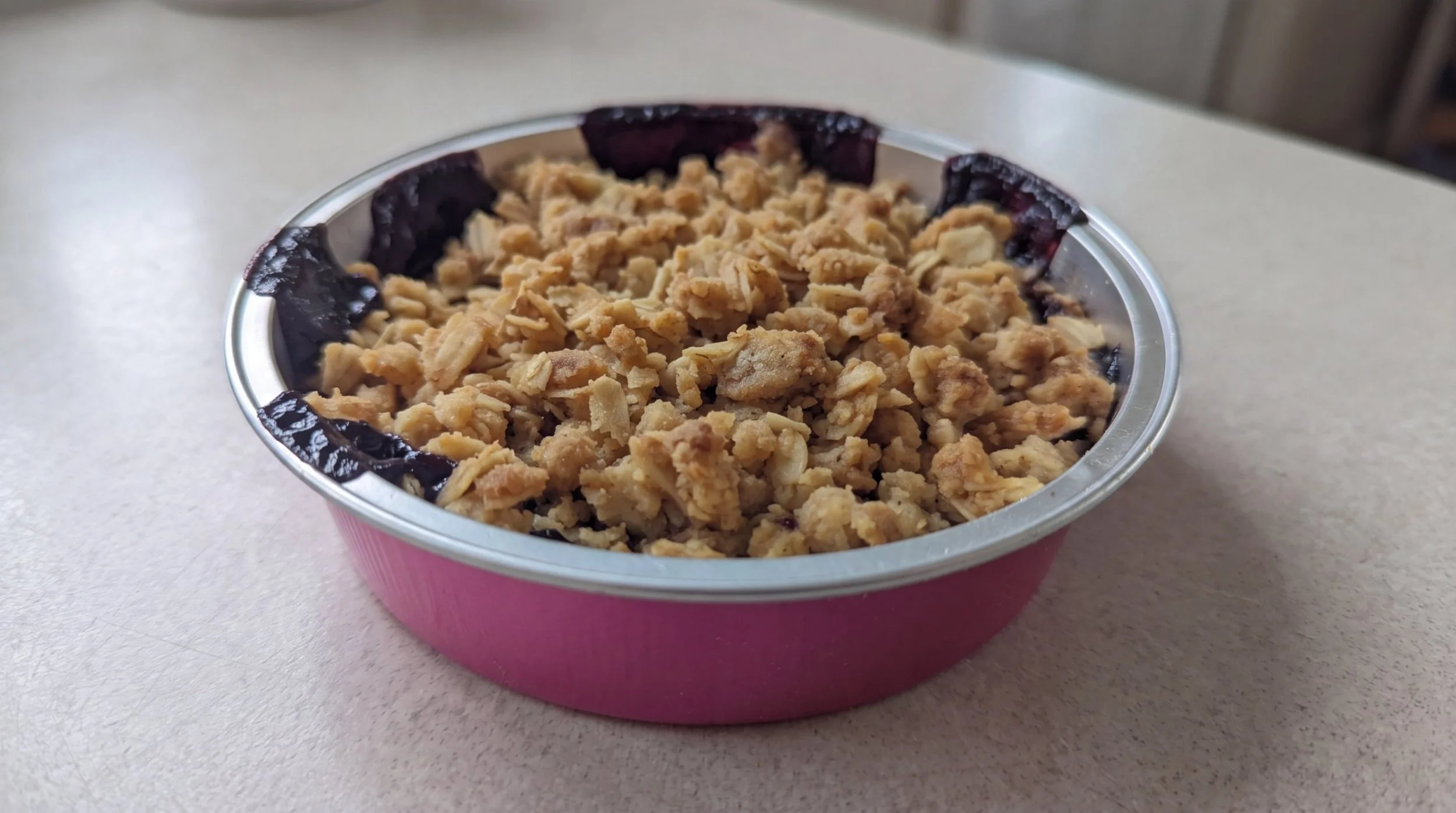 Baked blueberry crisp with crumble topping in a round pink tin
