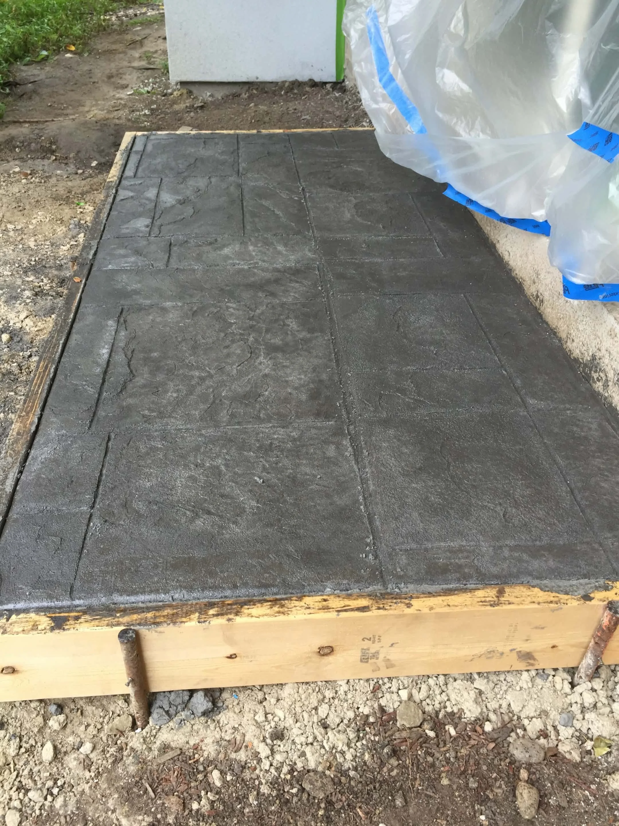 Freshly poured concrete patio with a stamped pattern, surrounded by wooden form boards, at an outdoor construction site.