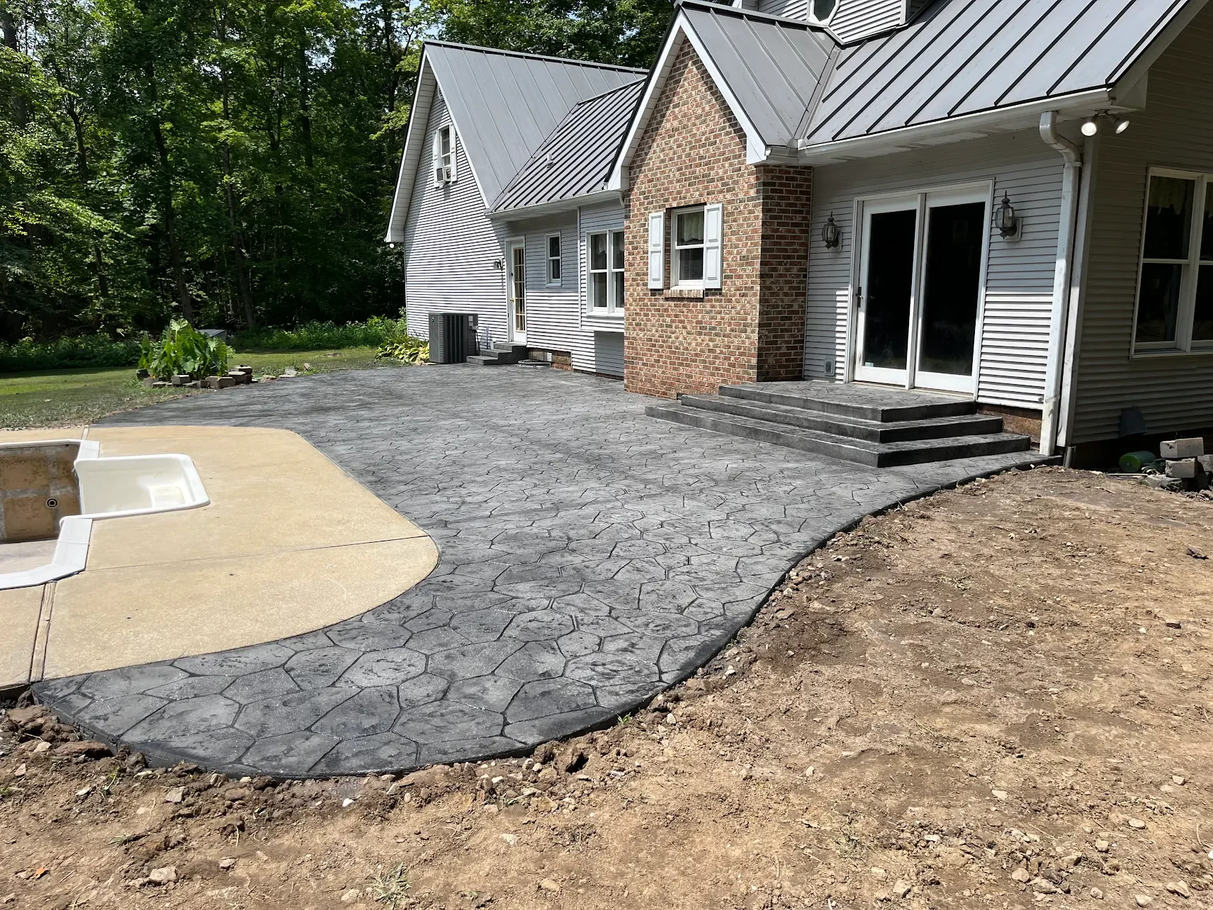 Backyard patio with stamped concrete, steps leading to sliding glass door, and a small section of unfinished yard with dirt.