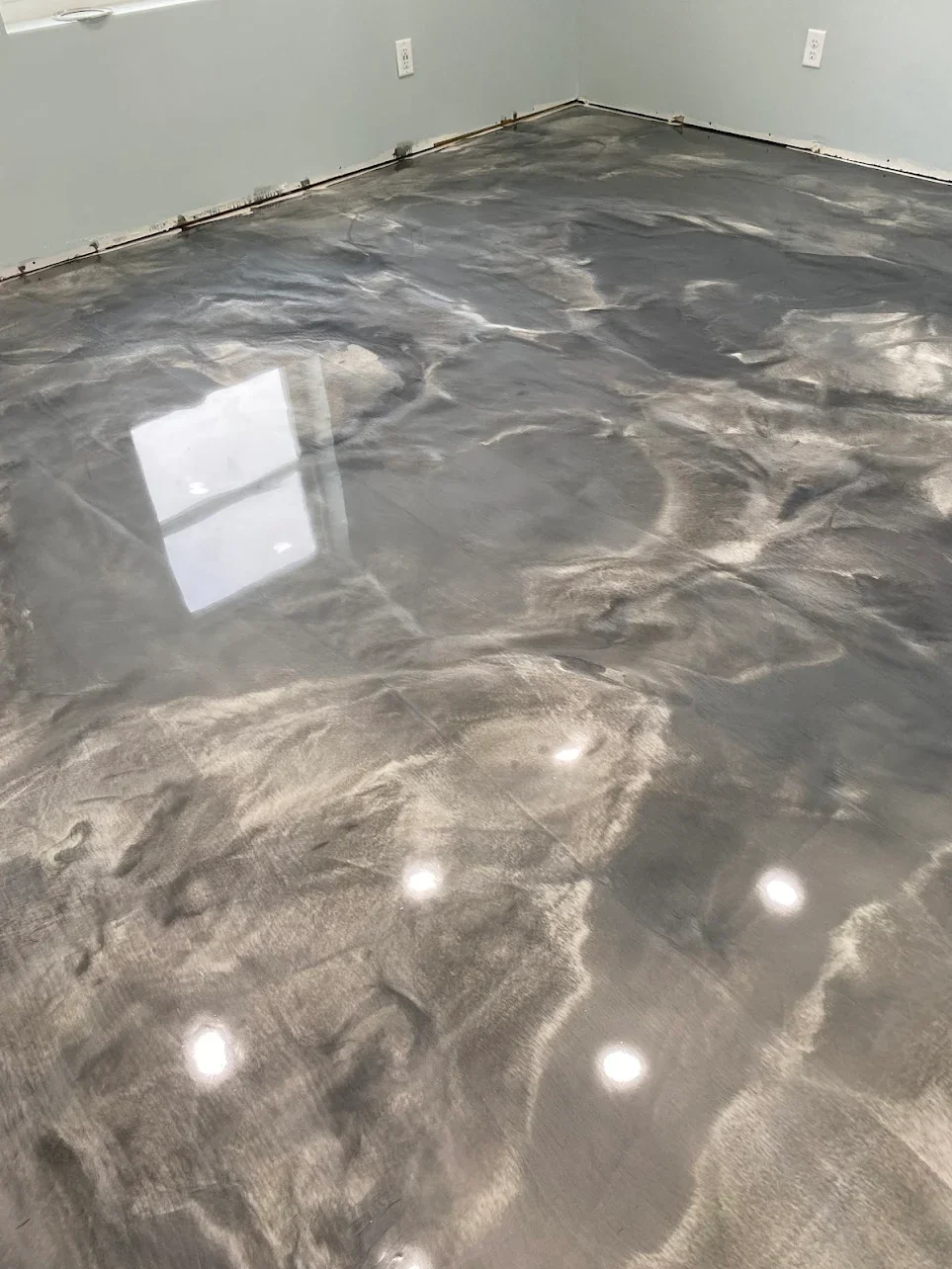 Polished concrete floor with a marble-like pattern and reflections of ceiling lights and a window.