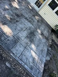 Newly poured and stamped custom gray concrete stone patio outside a house with beige siding and white trim by Rooks Construction and custom concrete.