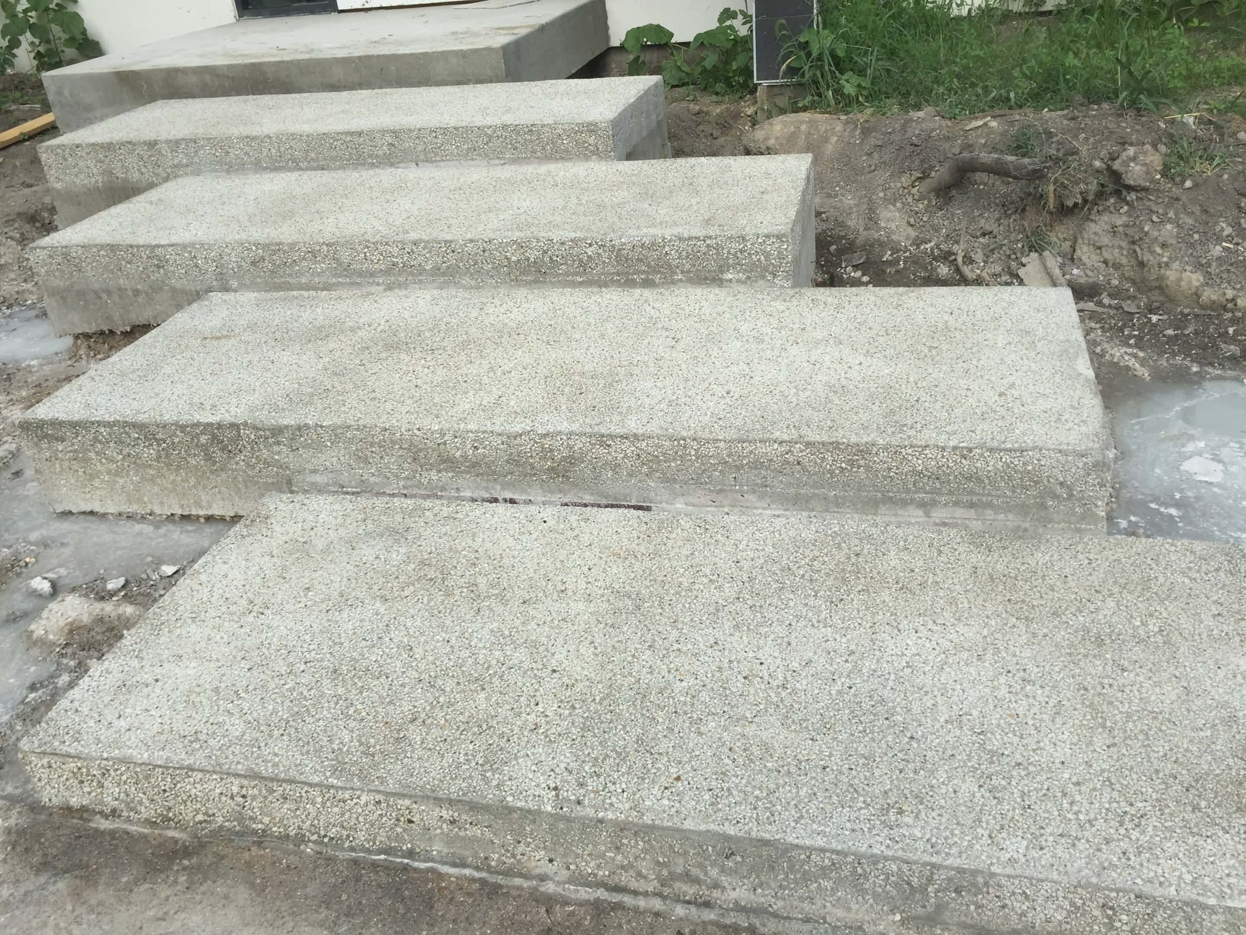 Concrete stairs under construction with five large concrete slabs placed on the ground, surrounded by dirt and some green plants.