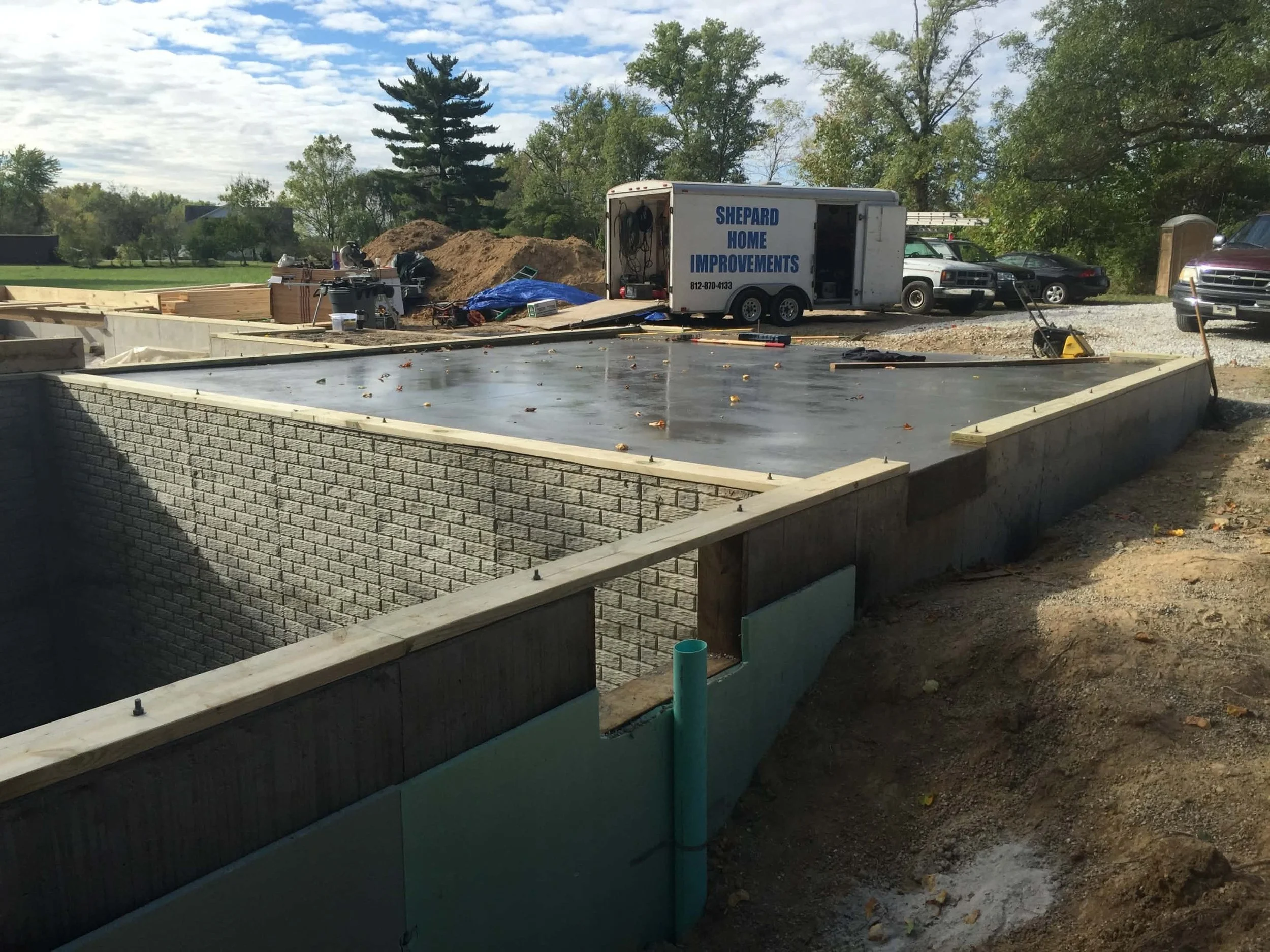 Construction site with a newly poured concrete foundation, brick walls, and construction equipment. 