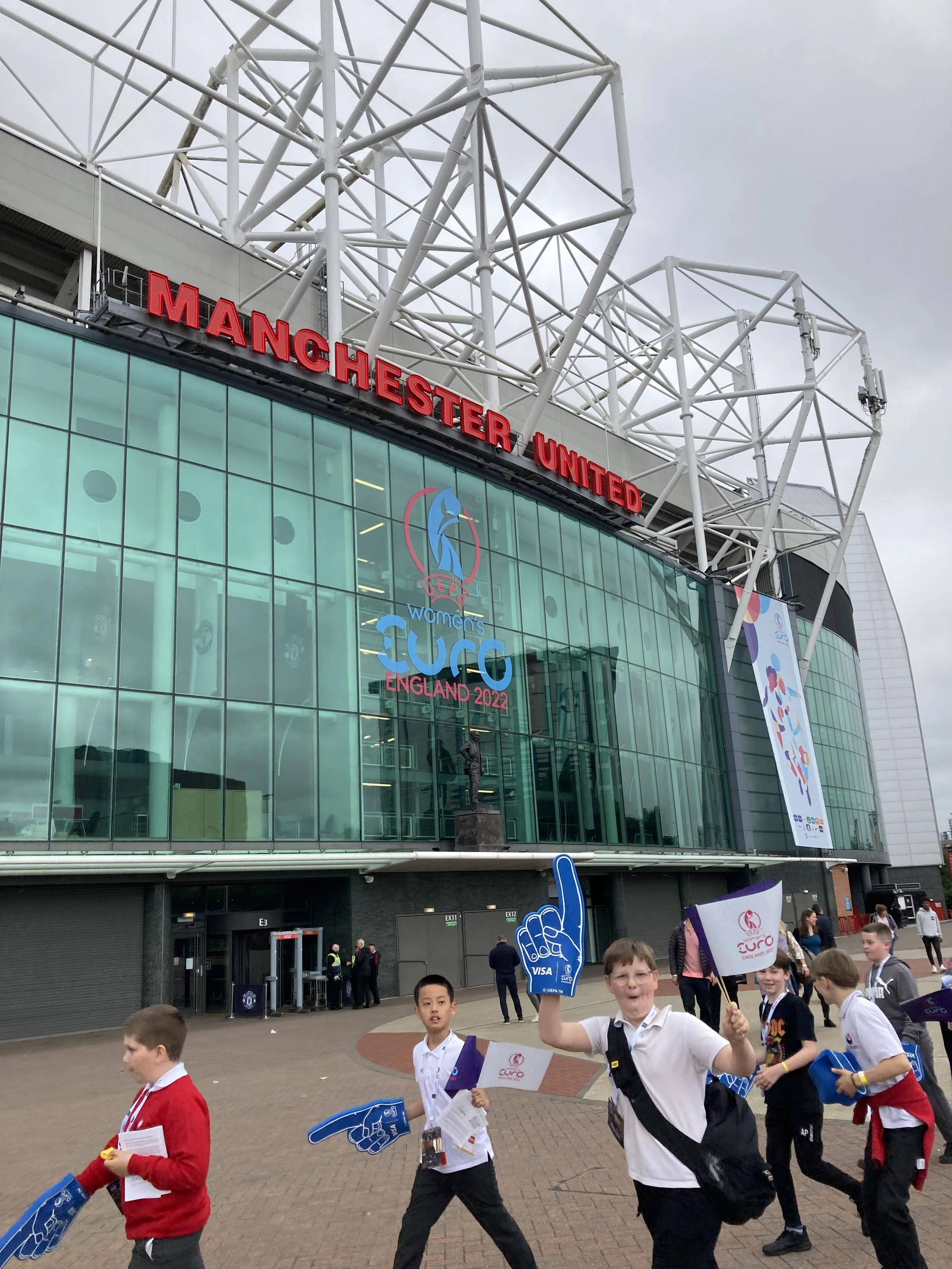 Image of a group of boys walking past the front of Old Trafford supporting the Womens Euros