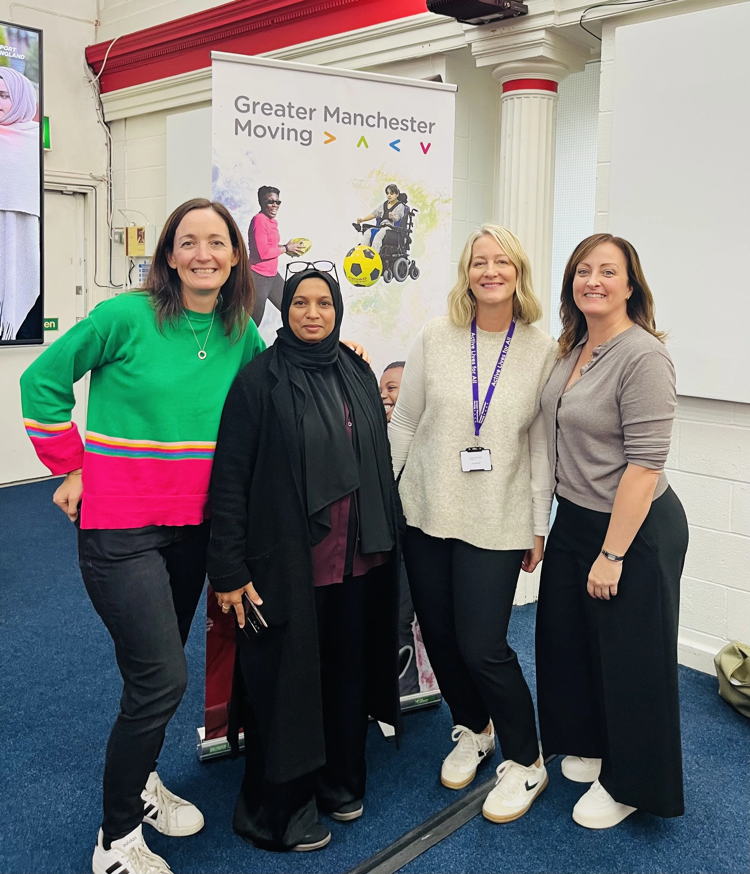 Group of 4 women infornt of a Greater Manchester Moving sign as part of the Tackling Health and Inequalities Network
