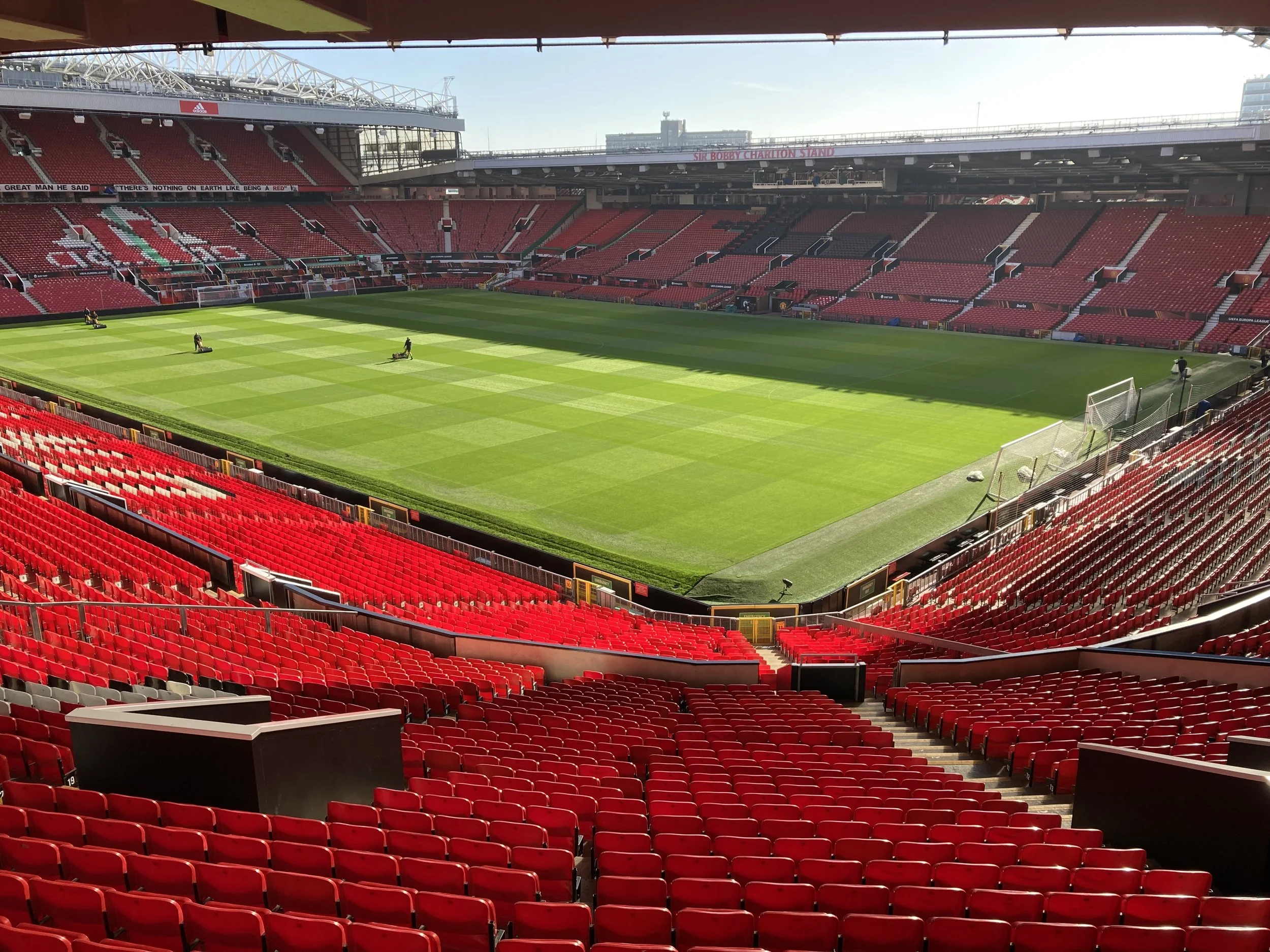 A picture of the pitch at Anfield. The stadium is empty but the sun is beaming down on the bright green pitch