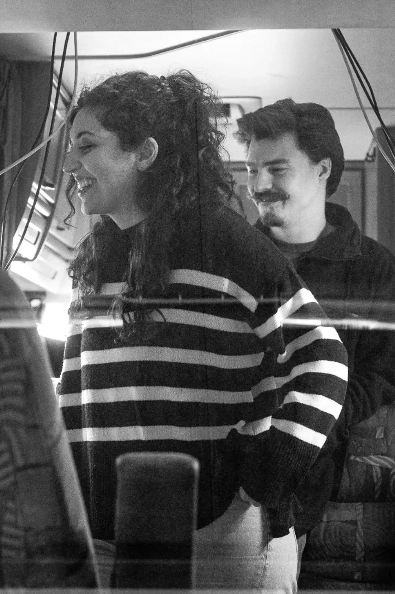 Twee mensen van bedrijf Motion Stream die glimlachen: een vrouw met krullend haar en een man met een baard en snor. Ze zijn te zien door een raam van een campervan waar ze in staan.