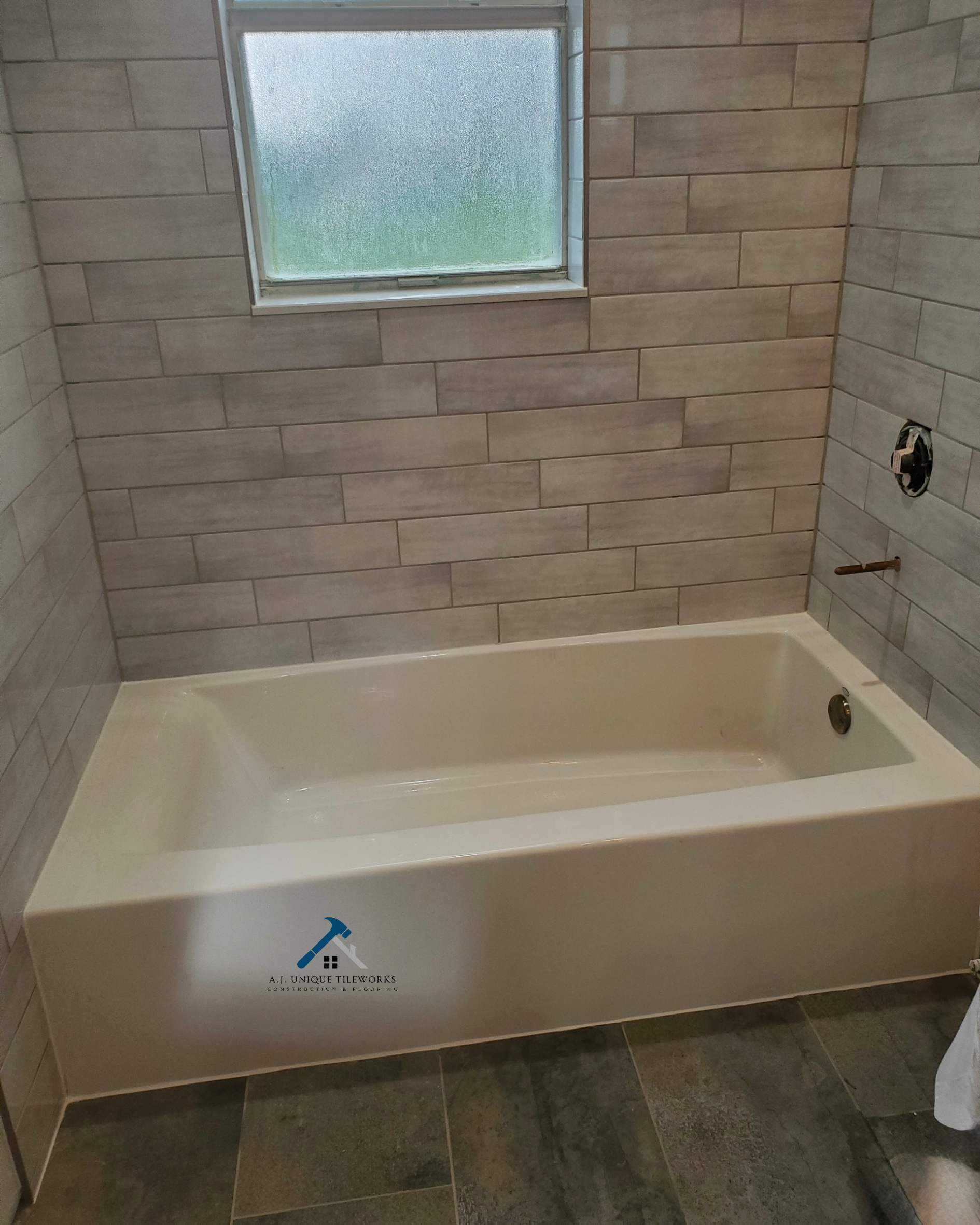 Bathroom with tile walls and a bathtub under a frosted window, with fixtures not yet installed.