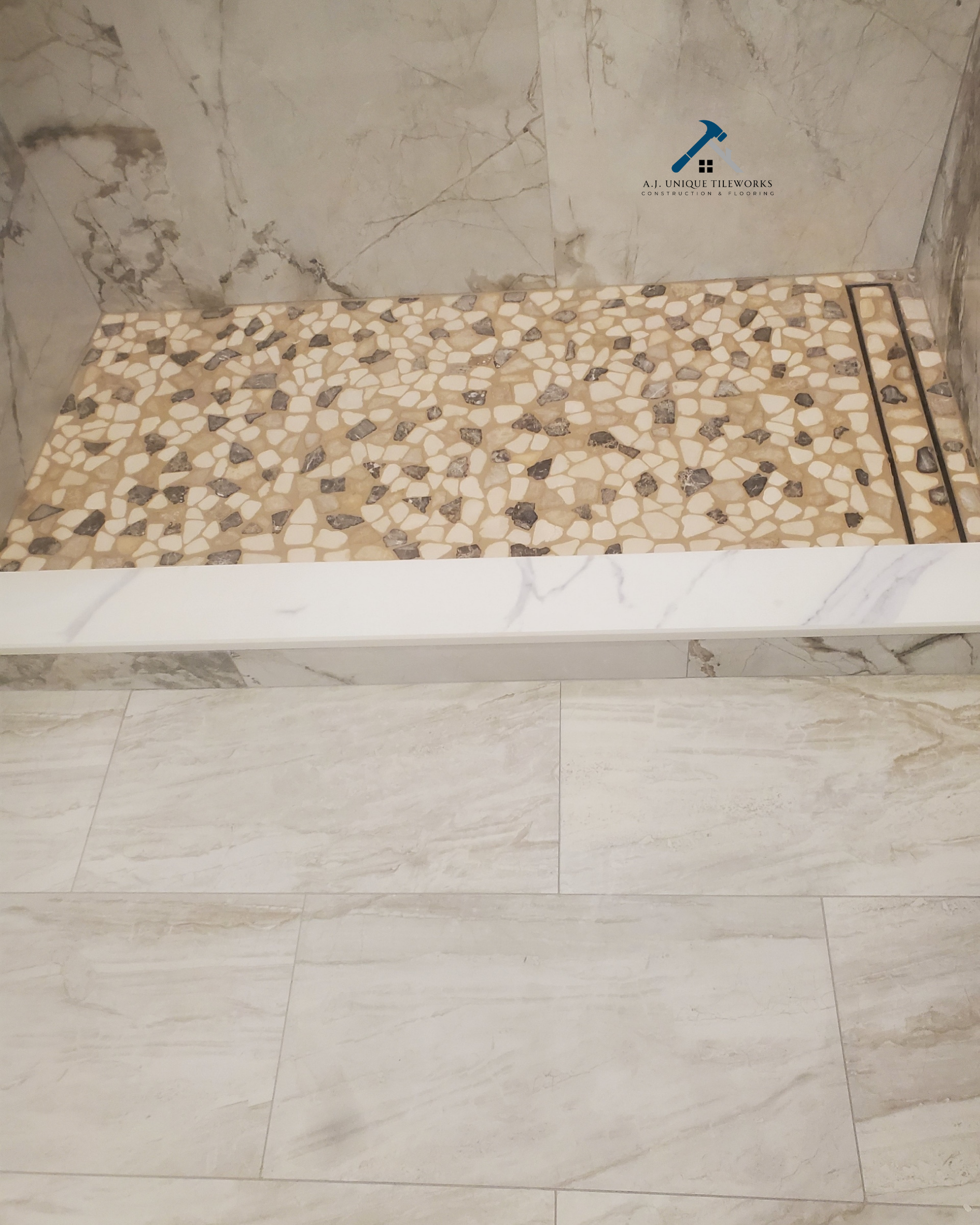 Close-up of a shower area with pebble tiles, marble walls, and marble flooring with a linear drain.