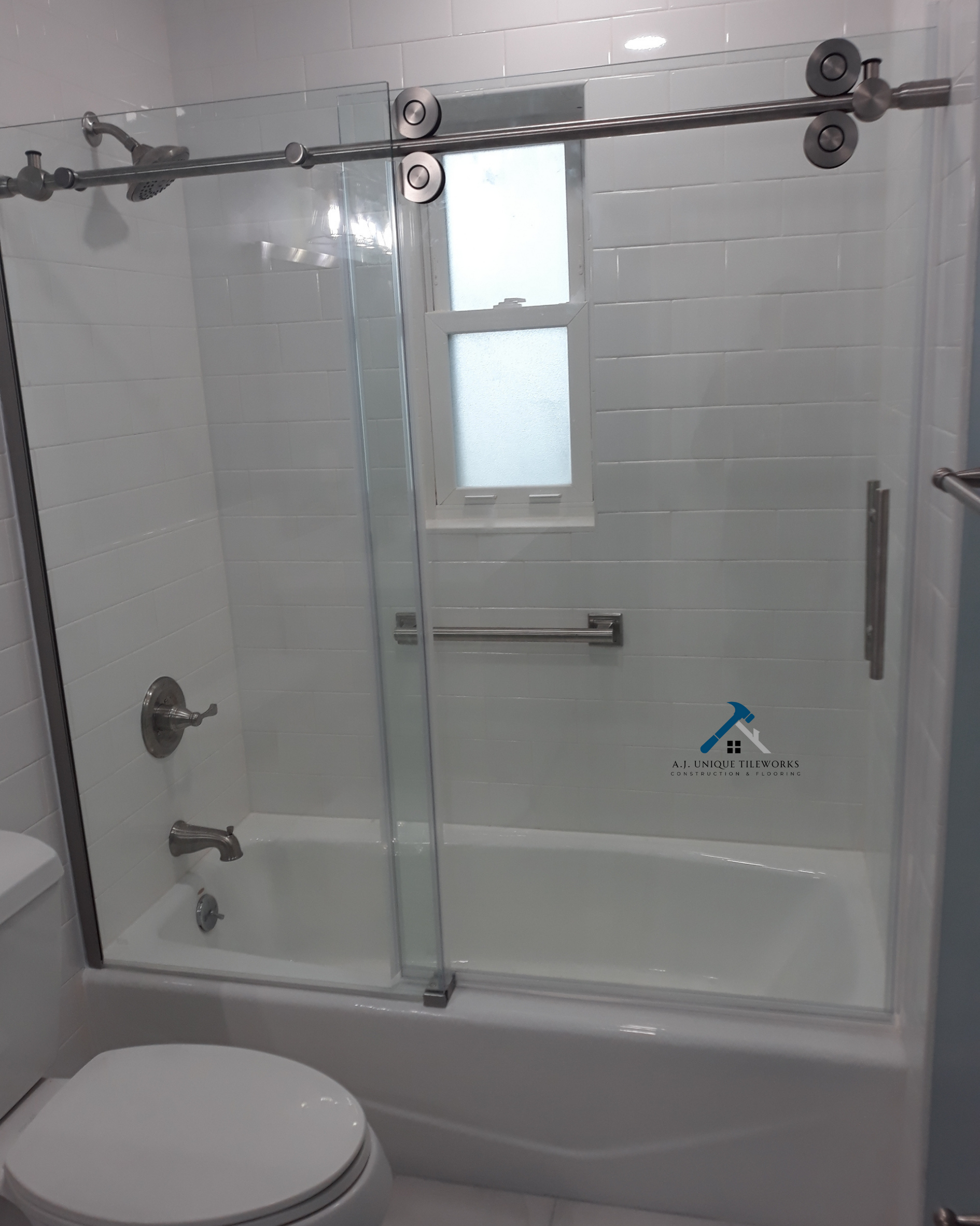 Bathroom with tub and shower area enclosed by glass sliding doors, a small frosted window, and white tiled walls