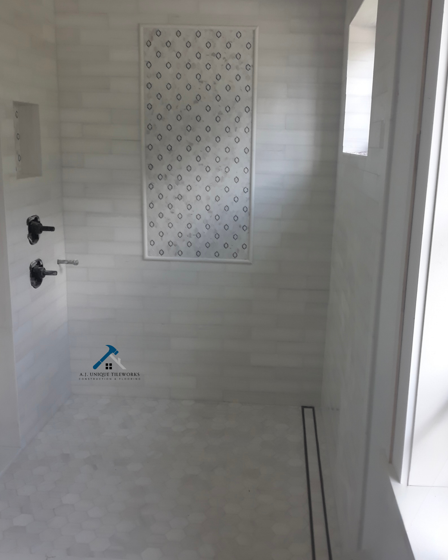 Empty shower with white subway tiles on the wall, hexagon floor tiles, and a small window with frosted glass. There are plumbing fixtures but no shower head installed yet.