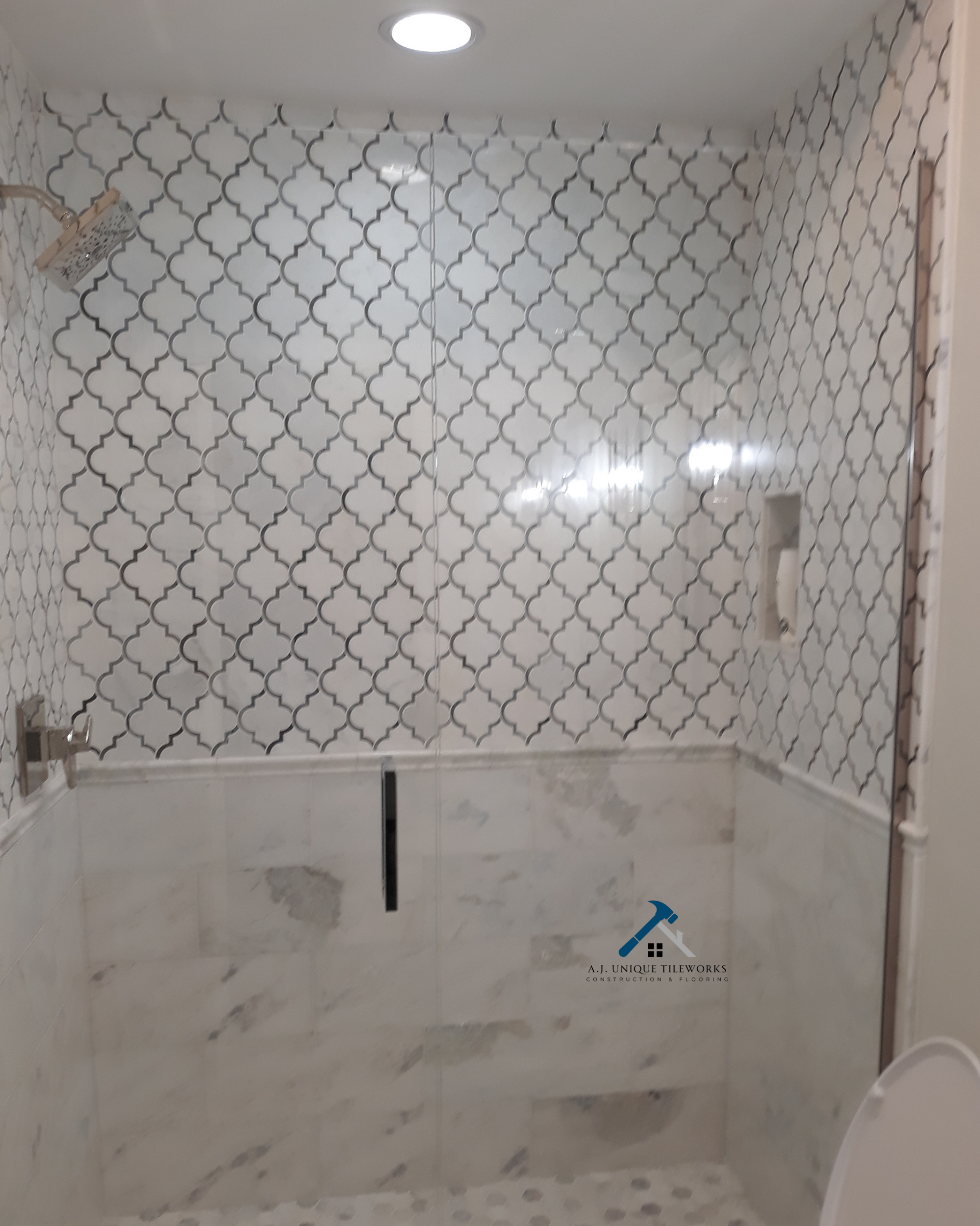 Bathroom with large mirror, patterned wall tiles, marble lower wall tiles, and a showerhead on the top left ceiling.