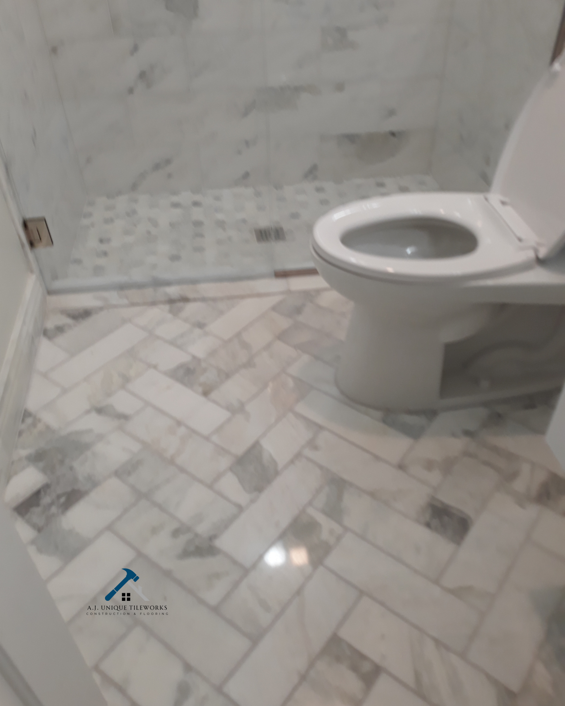 Bathroom with a toilet, marble tile flooring, and a shower area with marble tiles and a drain.