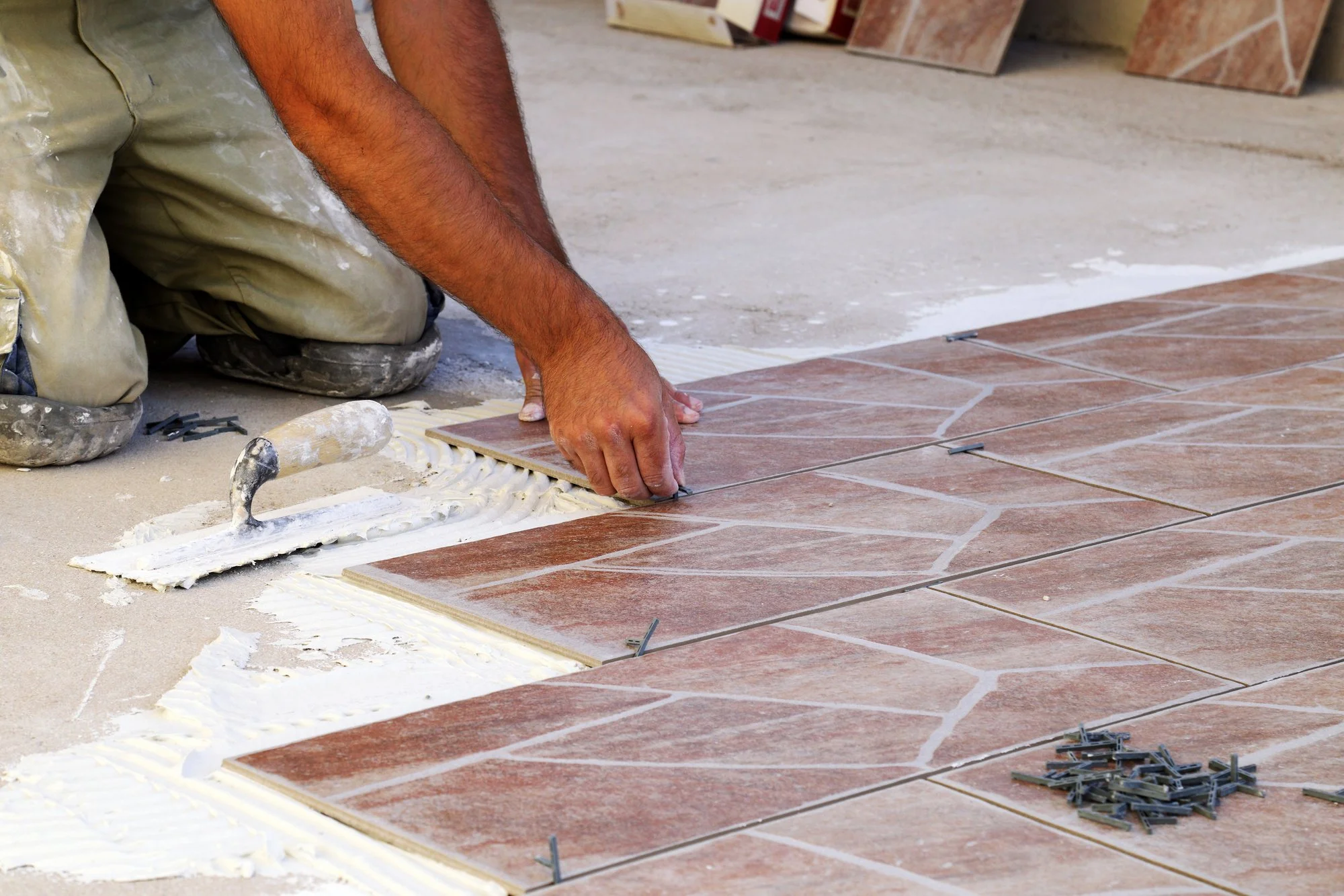 A person installing ceramic tiles on a floor, using spacers and trowel with white adhesive underneath the tiles.