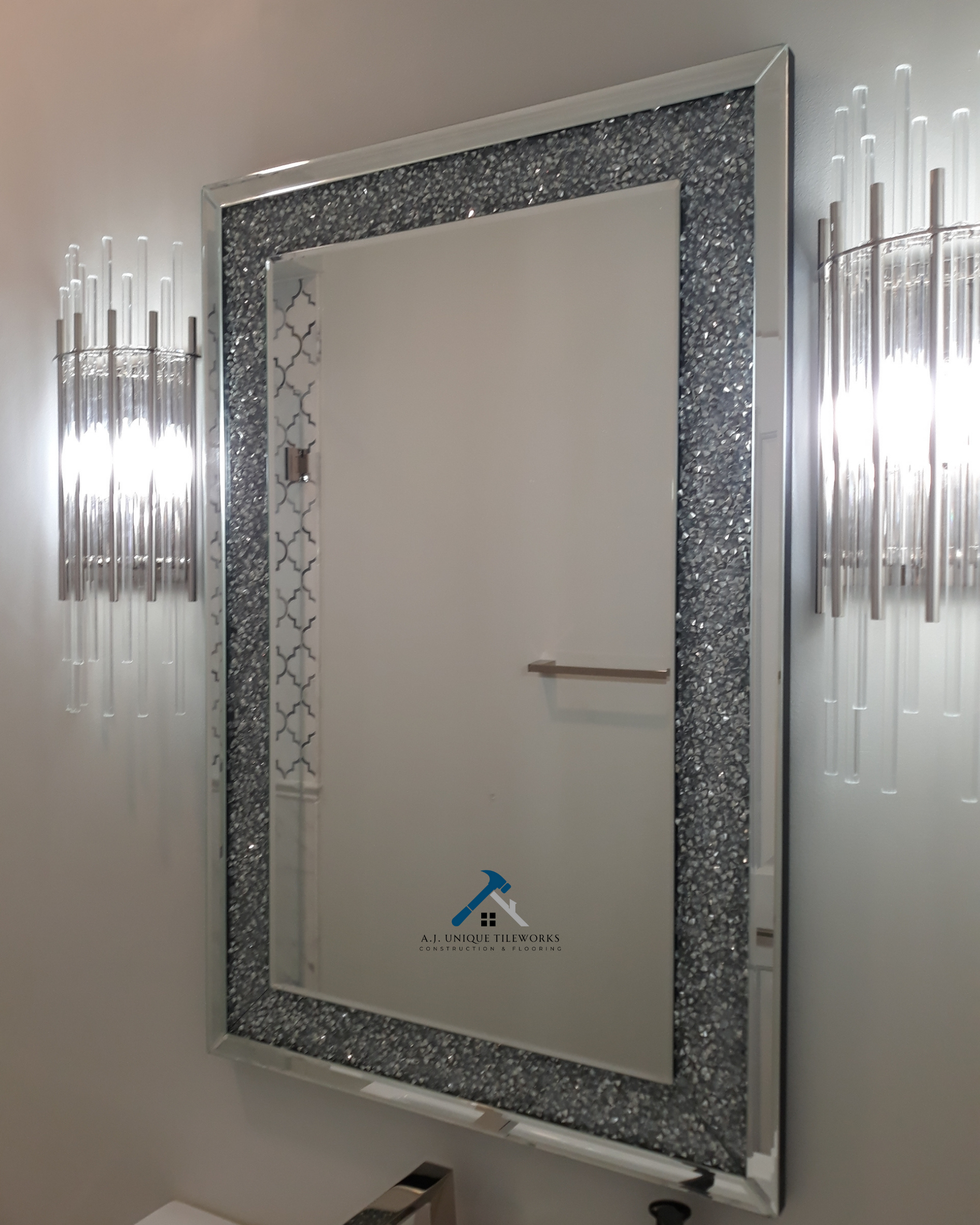 A decorative wall mirror with a sparkly, textured frame in a modern interior, with two unique metallic wall sconces on either side emitting bright light.