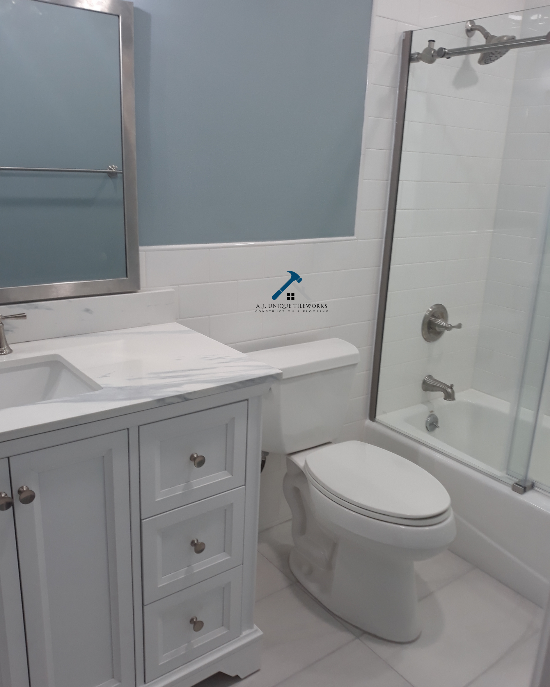 Bathroom with white vanity, toilet, and shower with glass door, white tiled walls, and blue painted wall above the tile