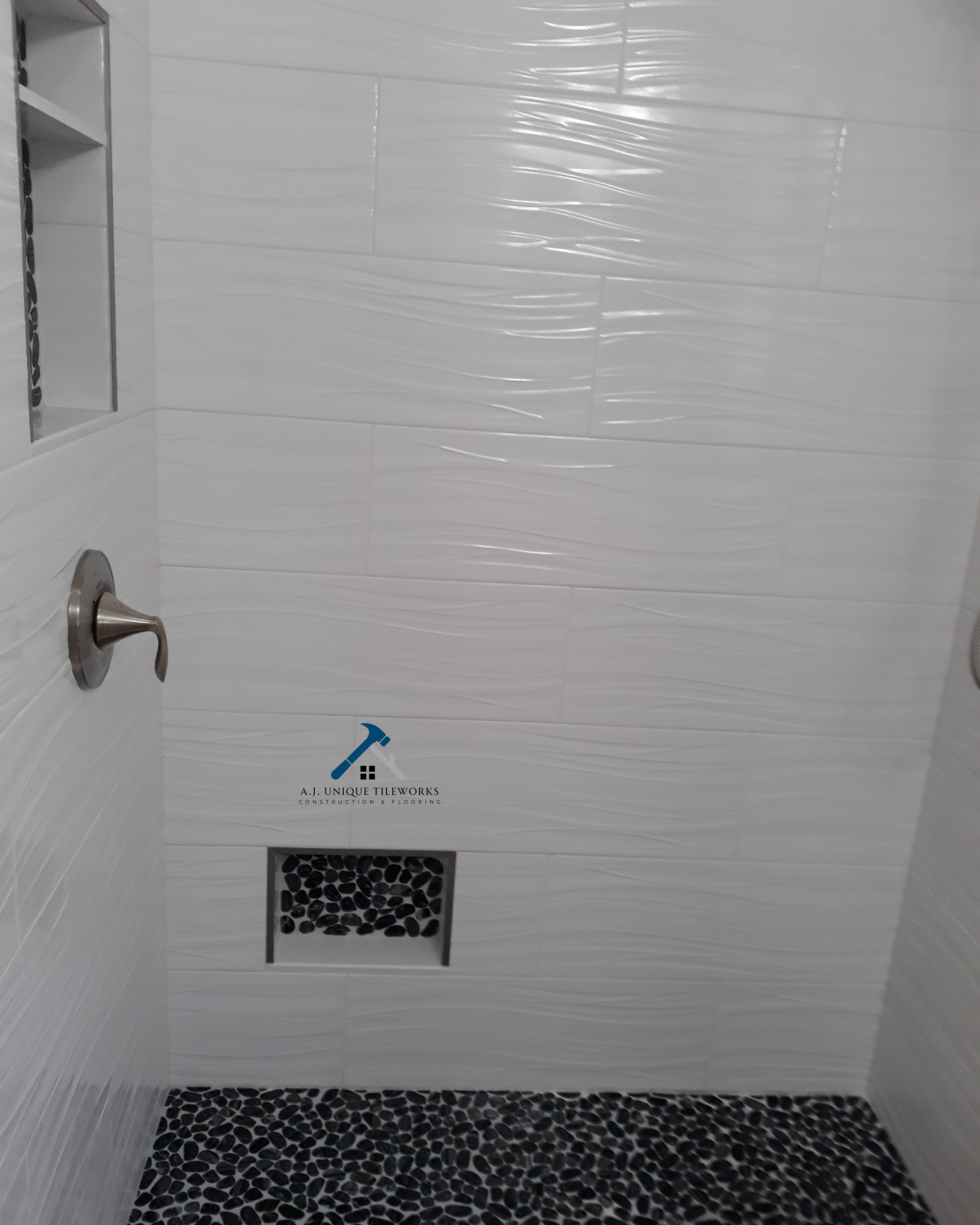Inside a modern shower with white textured tiles and pebble floor tiles, showcasing a wall drain, a built-in niche, and a shower faucet.