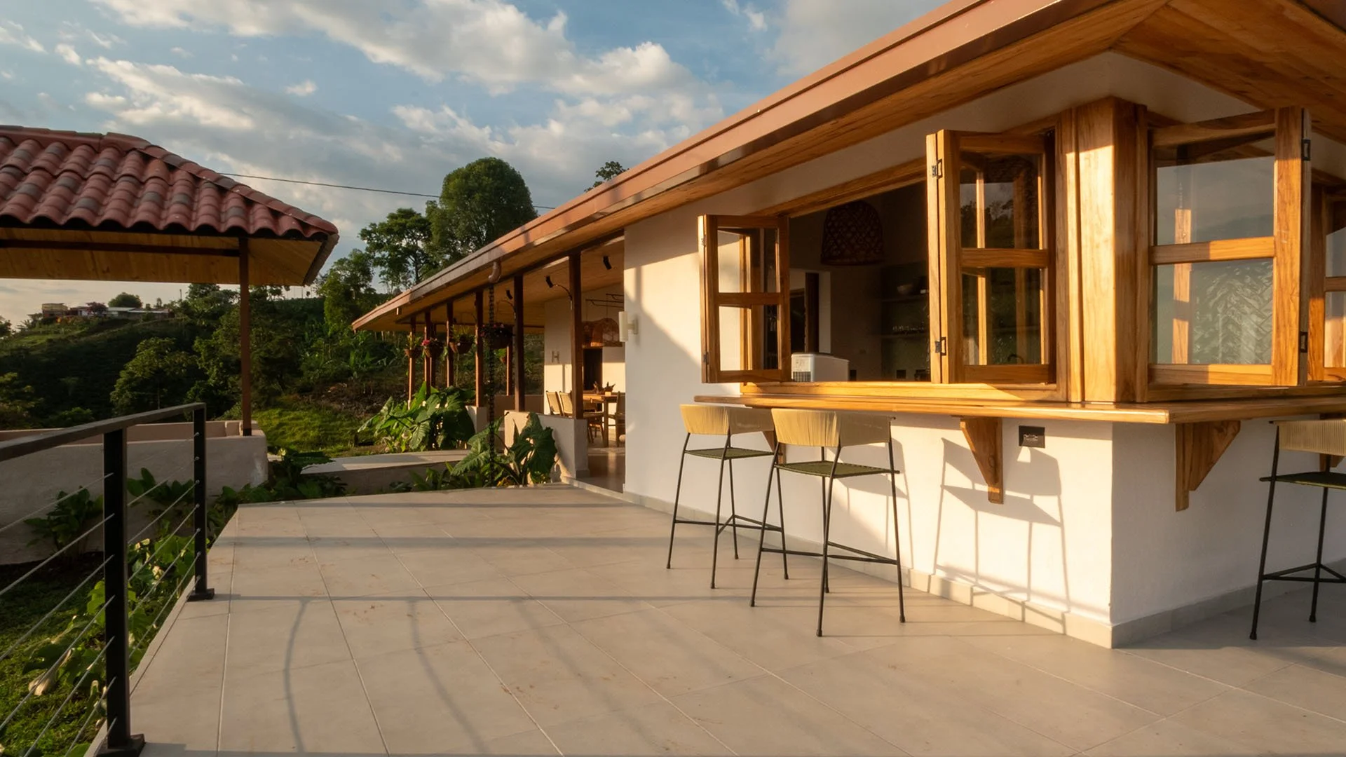 Terrraza con asientos y ventanas de madera, vista a áreas verdes y colinas, estilo rústico y moderno.