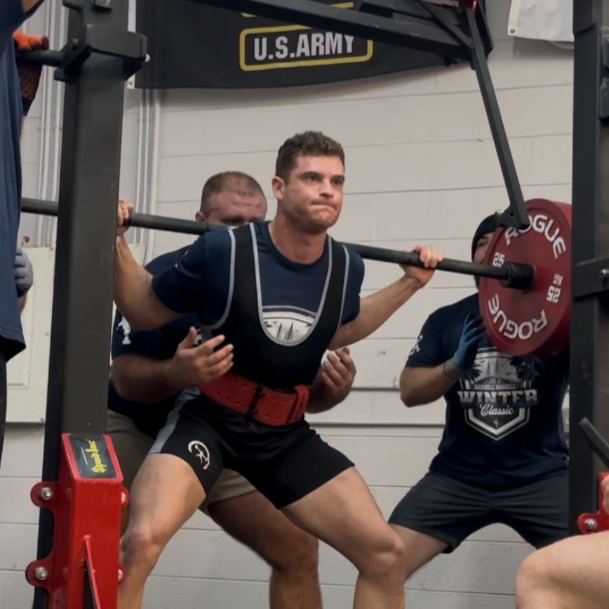 Man performing a barbell squat with weights under supervision in a gym with U.S. Army signage.