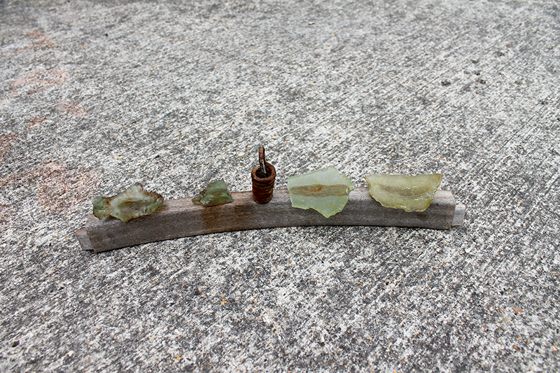Small pieces of greenish stone and a rusty nail on a wooden stick on concrete ground.