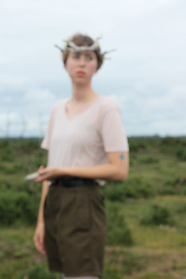 Woman wearing a crown made of branches standing outdoors in a grassy field.