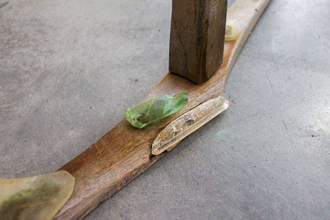 Close-up of a wooden structure with an old, dirty glass bottle and a green glass fragment on it, on a gray concrete floor.