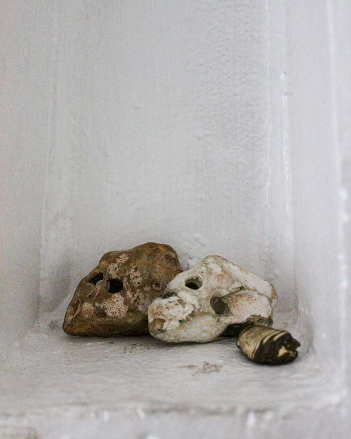 Two rocks with holes and a small shell on a white surface against a white wall.