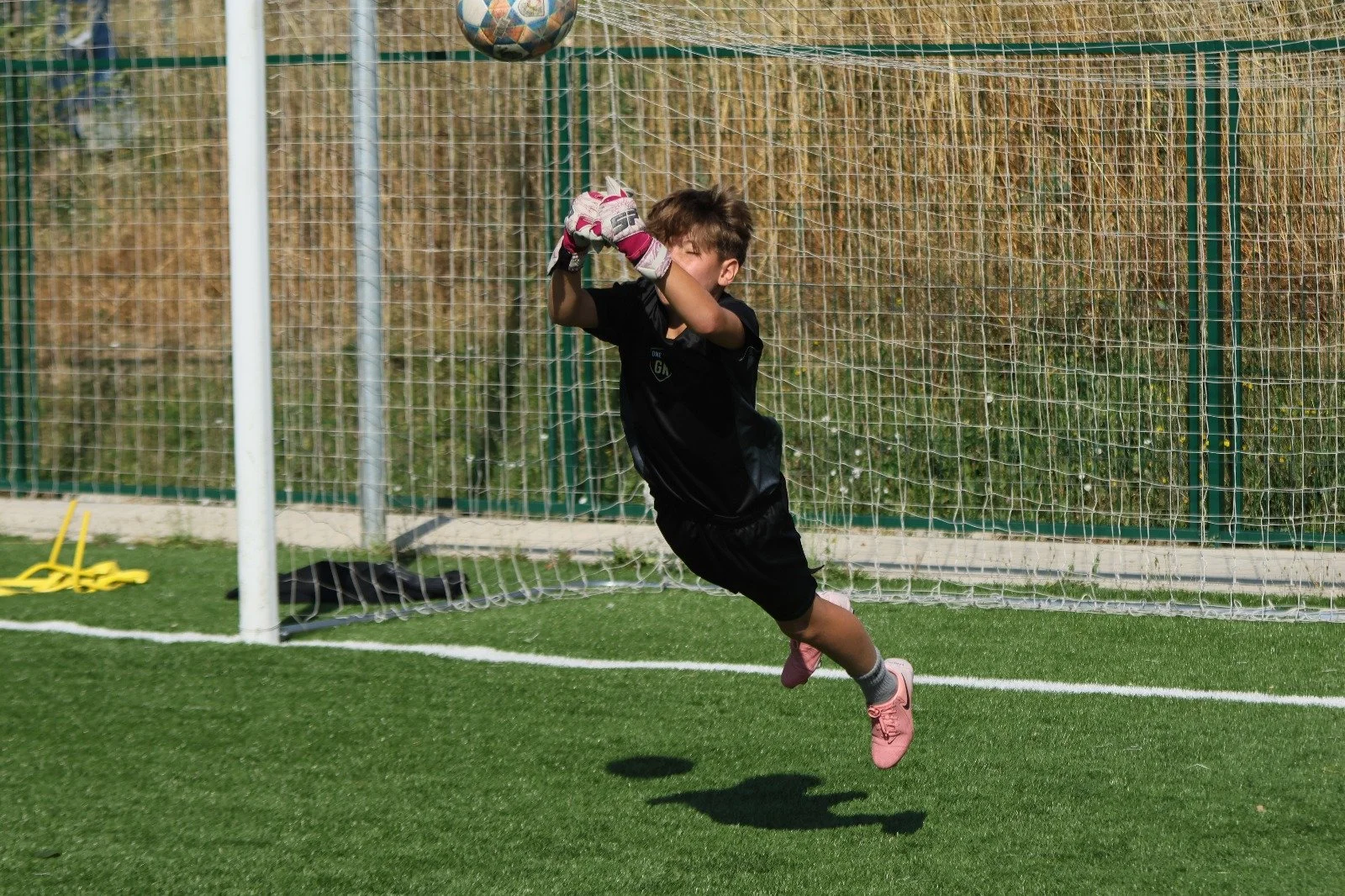 Niño arquero saltando en un campo de fútbol para detener un balón en la portería.