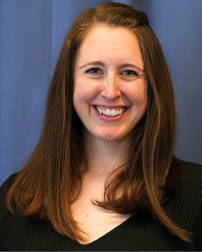 A woman with long brown hair smiling in front of a blue curtain.