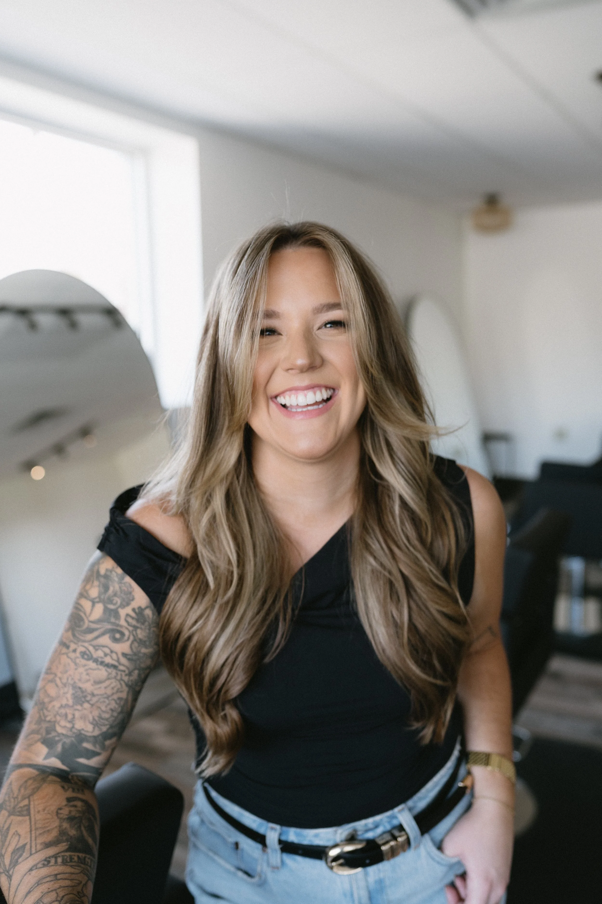 A woman with long wavy blonde hair smiling in a bright, modern room.