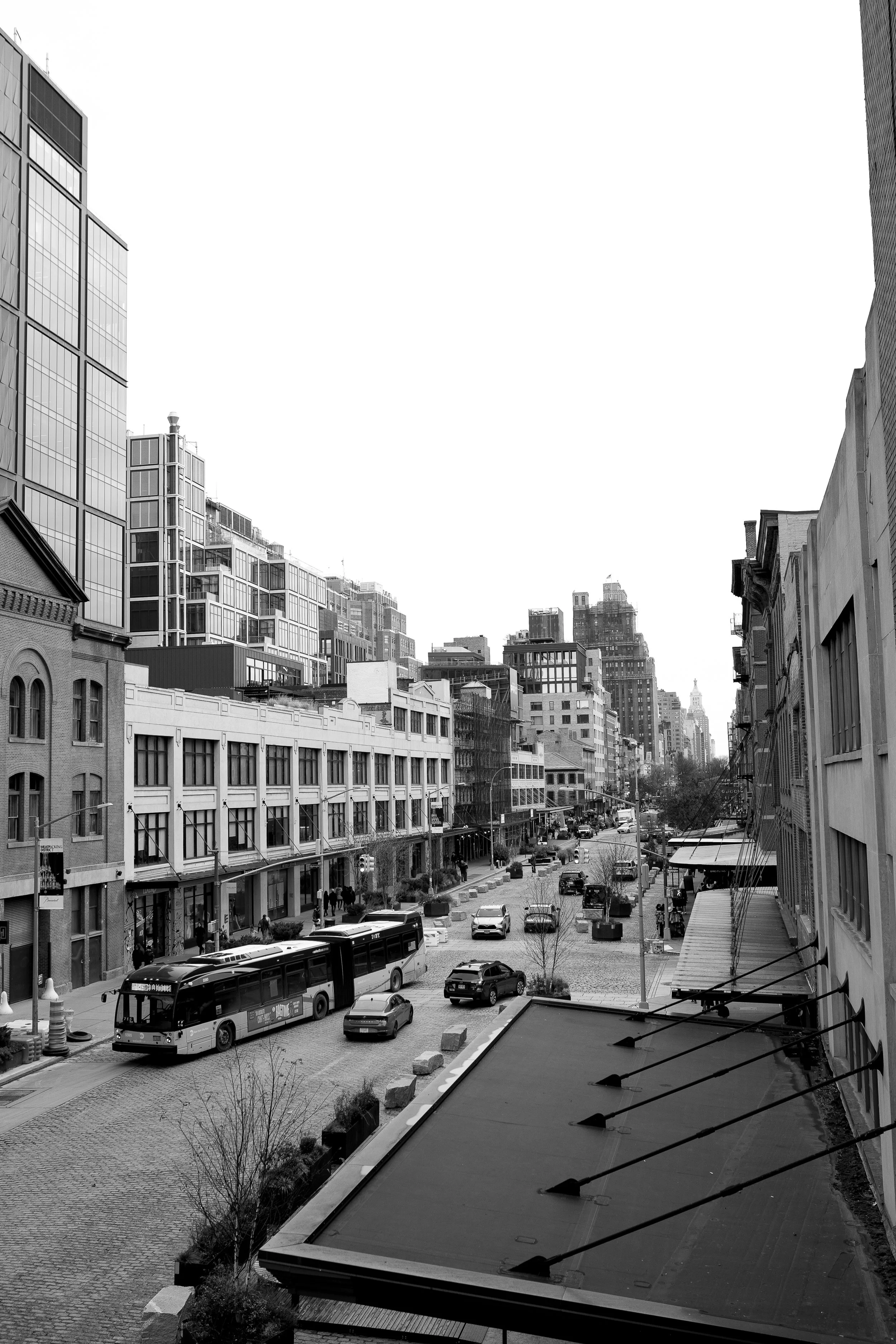 Black and white city street scene with cars, buses, buildings, and pedestrians.