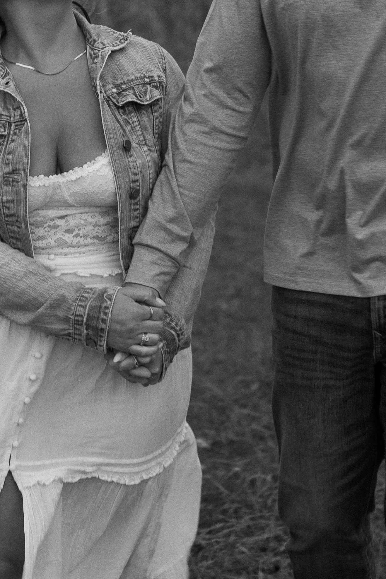 A couple holding hands, with the woman's hand resting on top of the man's hand, taken outdoors.