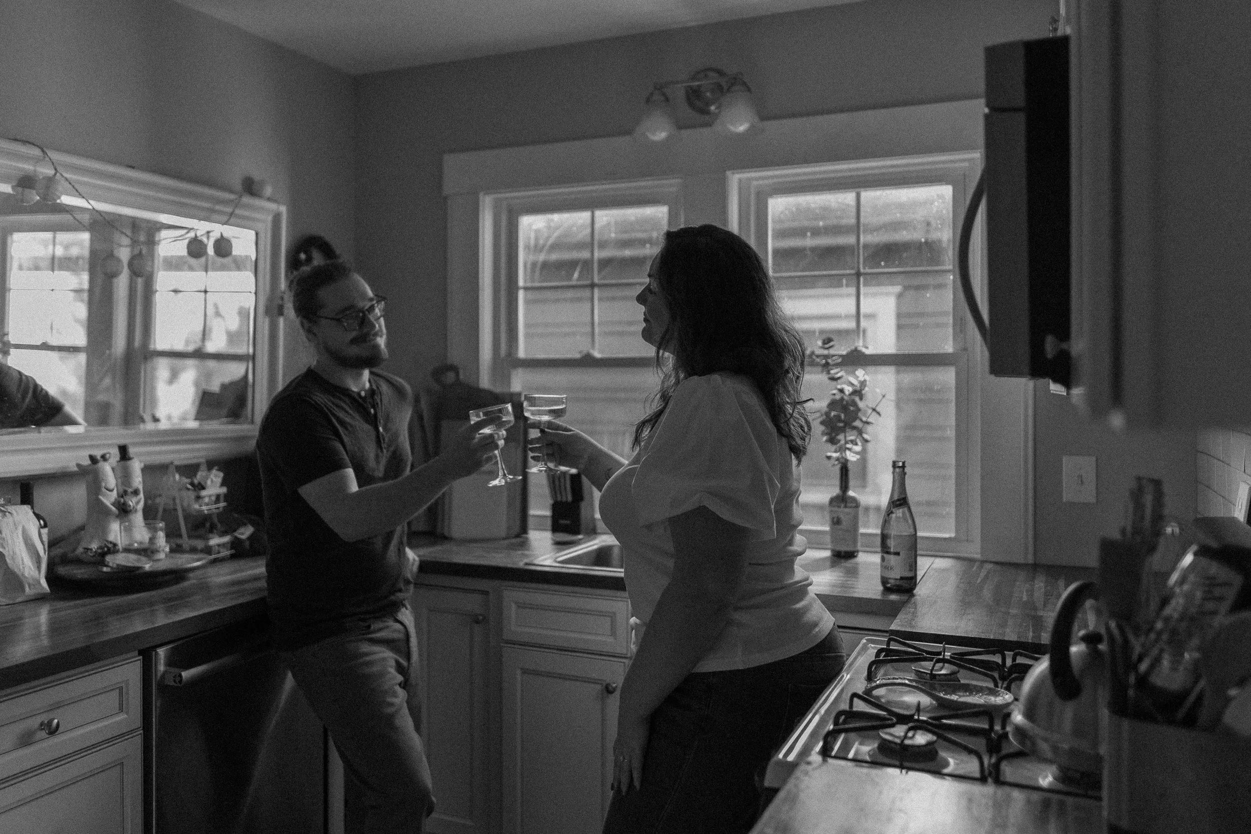 A man and woman toast with champagne glasses in a kitchen, sharing a moment of celebration.