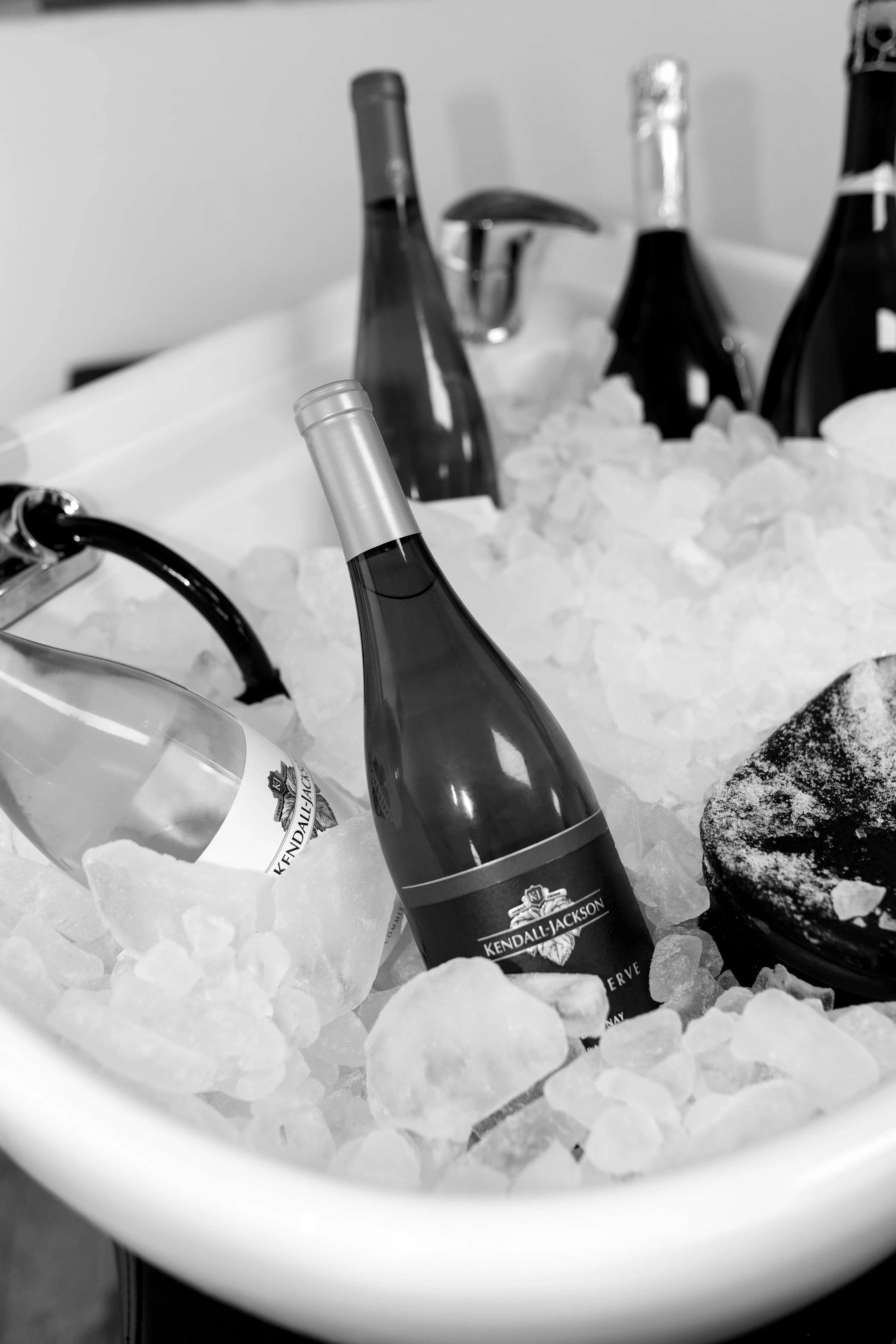 Chilled bottles of Kendall Jackson wine in ice cooler with wine glasses and a black plate.