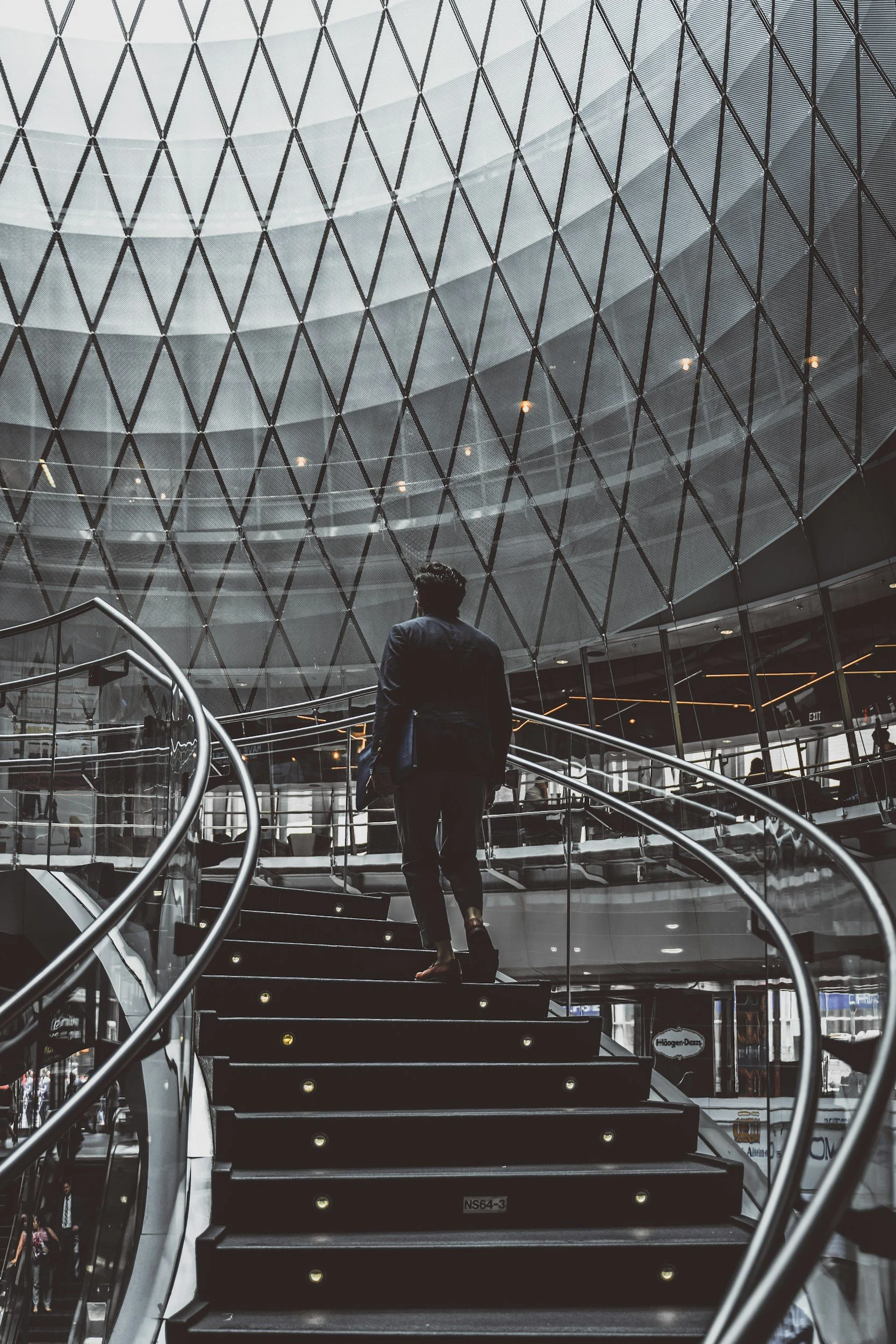 A man in a suit walking up a staircase inside a modern building with glass and metal architecture.