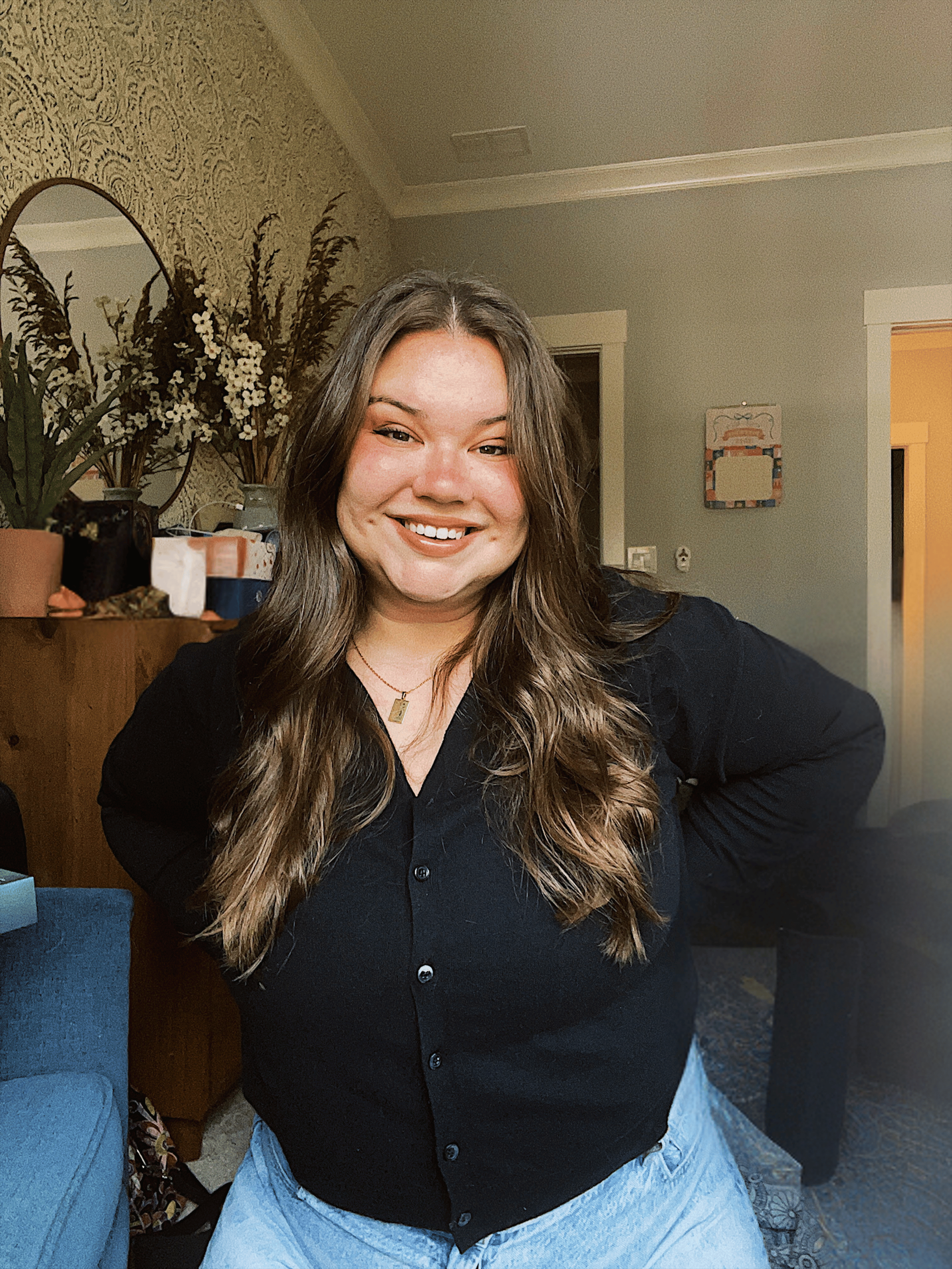 A woman with long wavy brown hair smiling and posing in a living room.