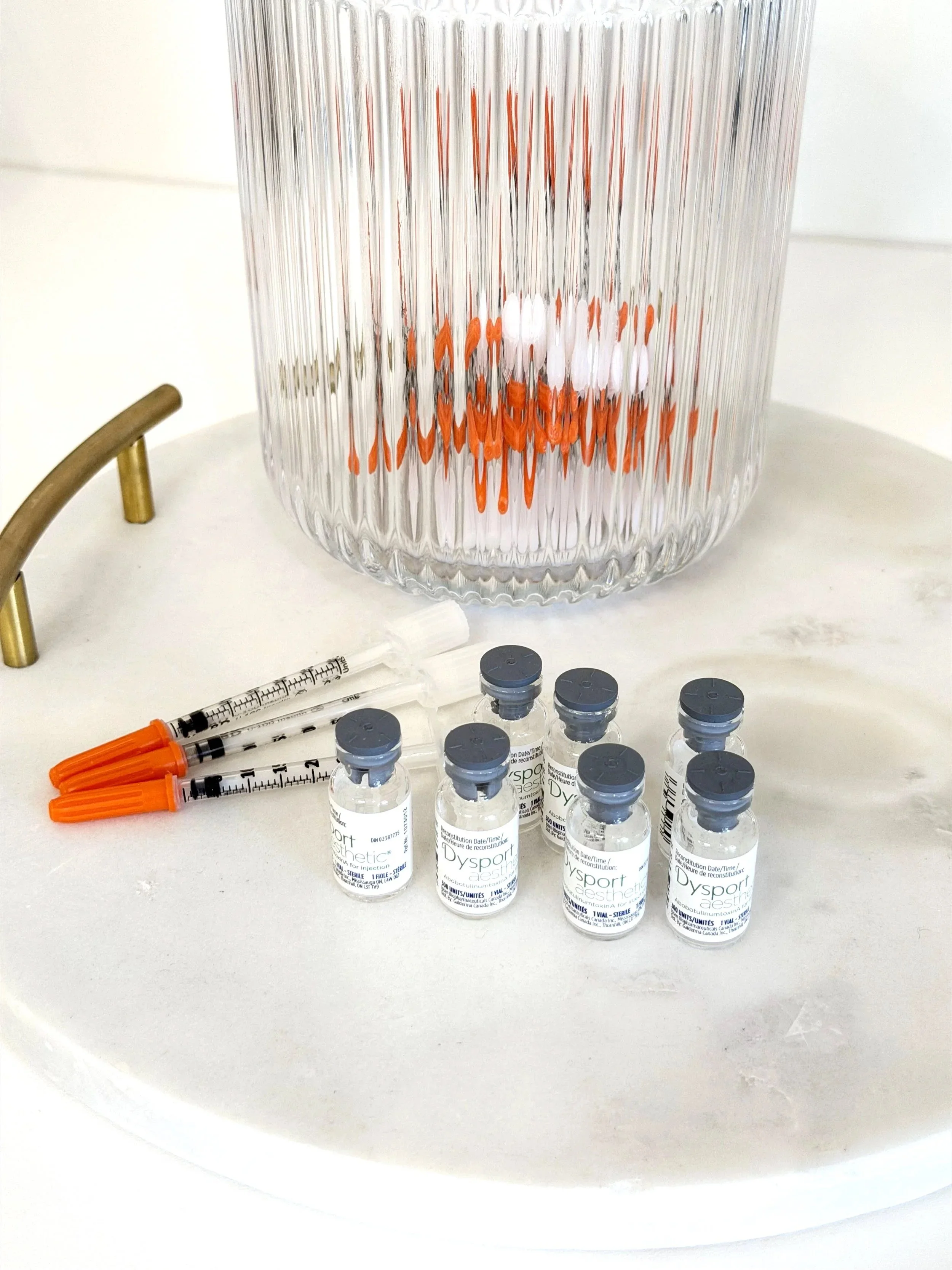Medical vials, syringes, and medical equipment arranged on a white surface in front of a decorative glass vase.