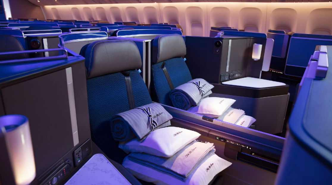 Two side by side United Polaris seats each with a stack of Saks 5th Avenue bedding