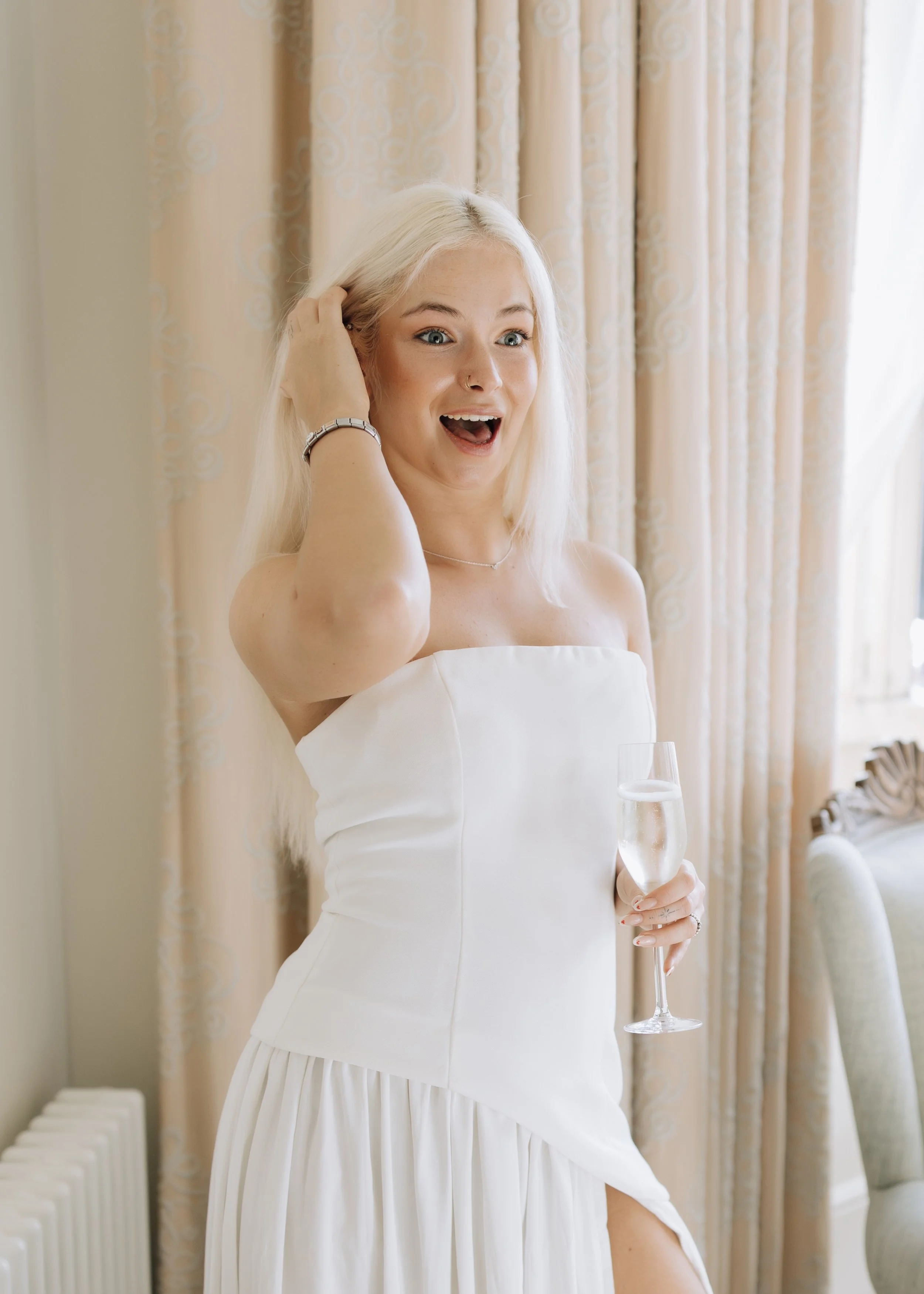 A woman in a white dress holding a glass of champagne, smiling and celebrating.