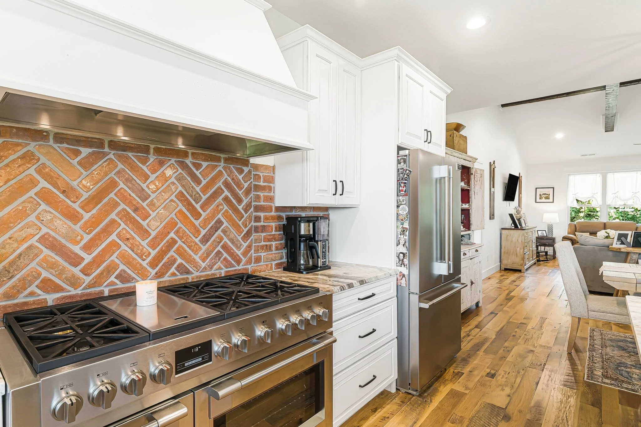 Kitchen area with a stainless steel stove, white cabinets, brick backsplash, black coffee maker, and a refrigerator in a cozy living space.