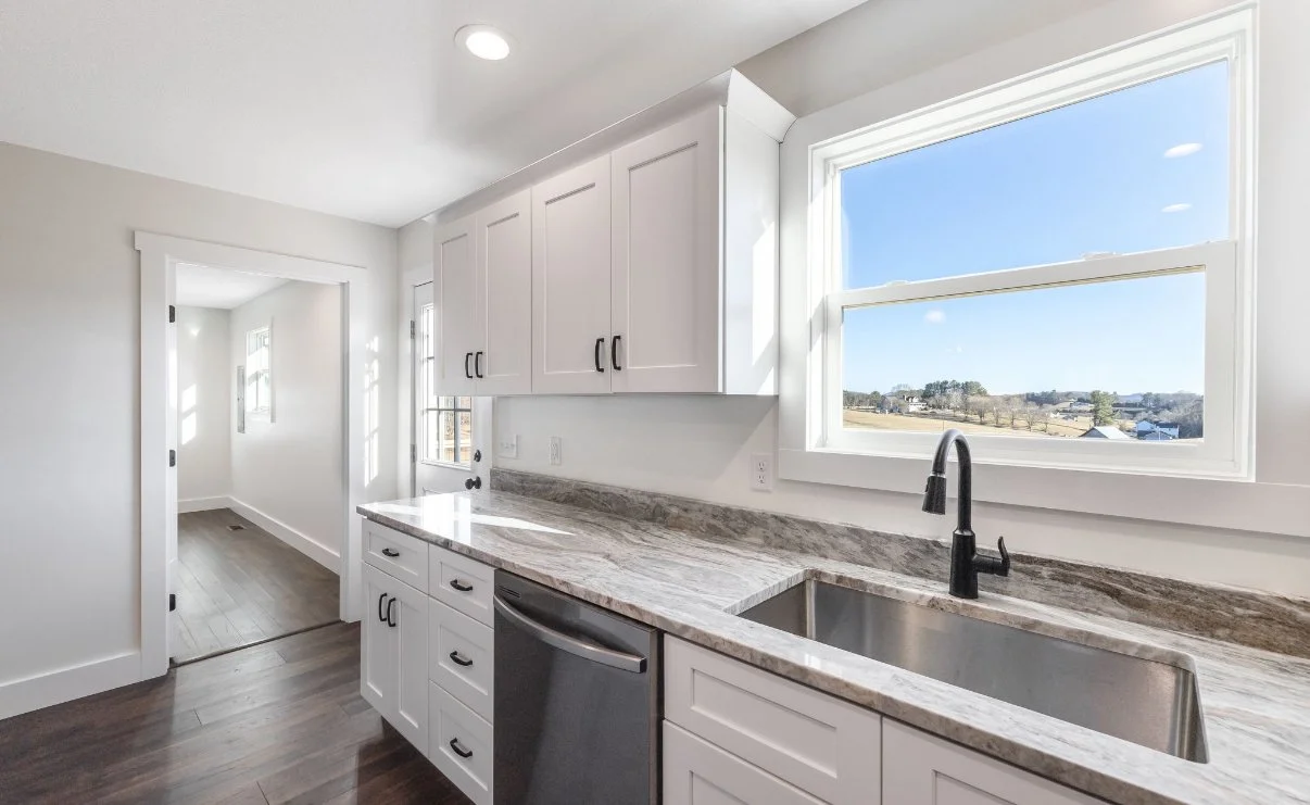 Kitchen with white cabinets, a granite countertop, and a large window overlooking a rural landscape.