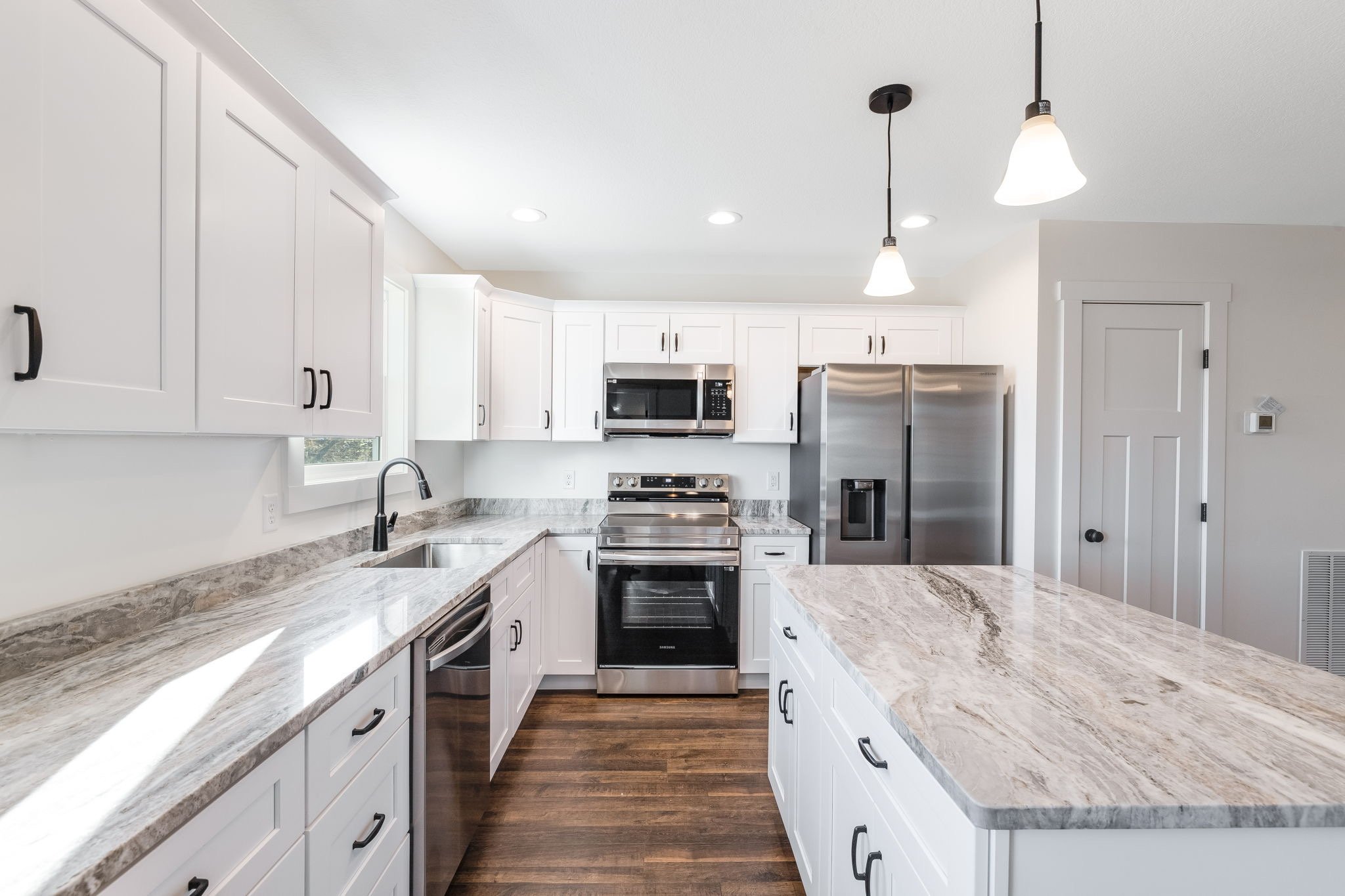 Kitchen with white cabinets, gray granite countertops, stainless steel appliances, hardwood floor, and pendant and recessed lighting.