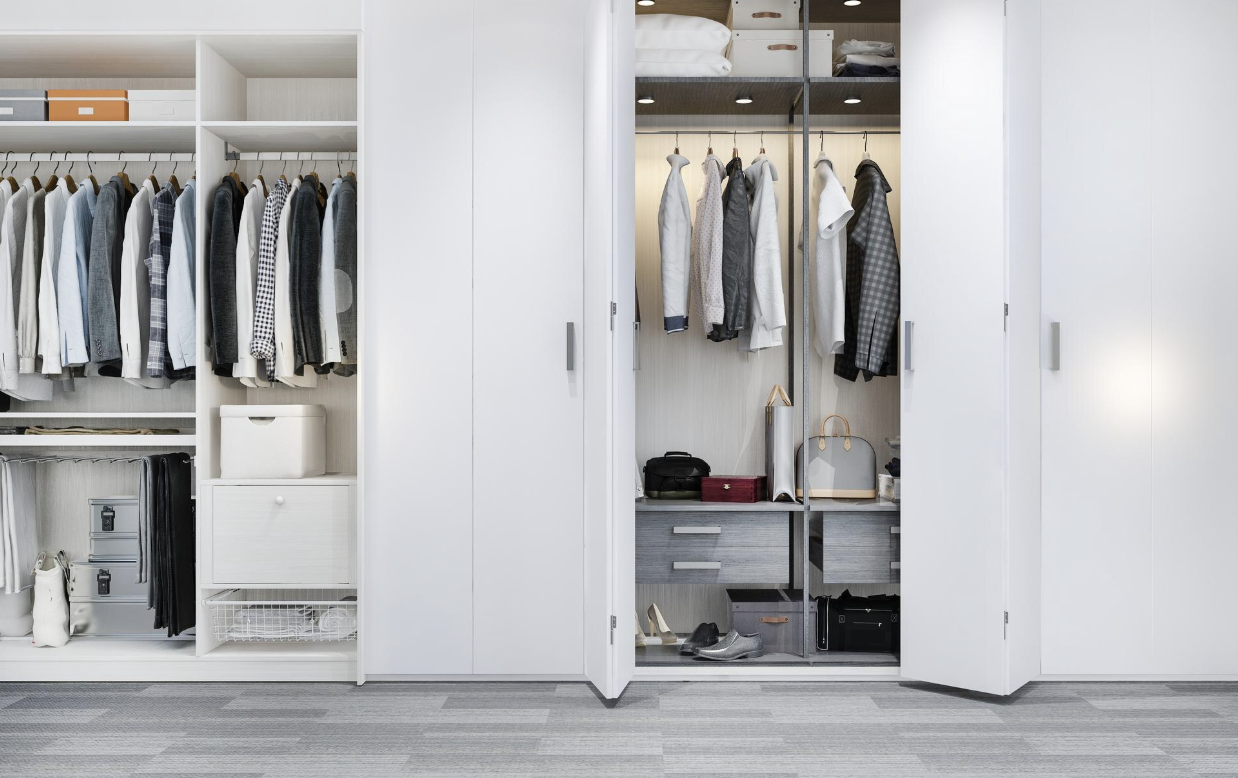 Open white closet doors revealing hanging clothes, shoes, and storage boxes inside a modern bedroom closet.
