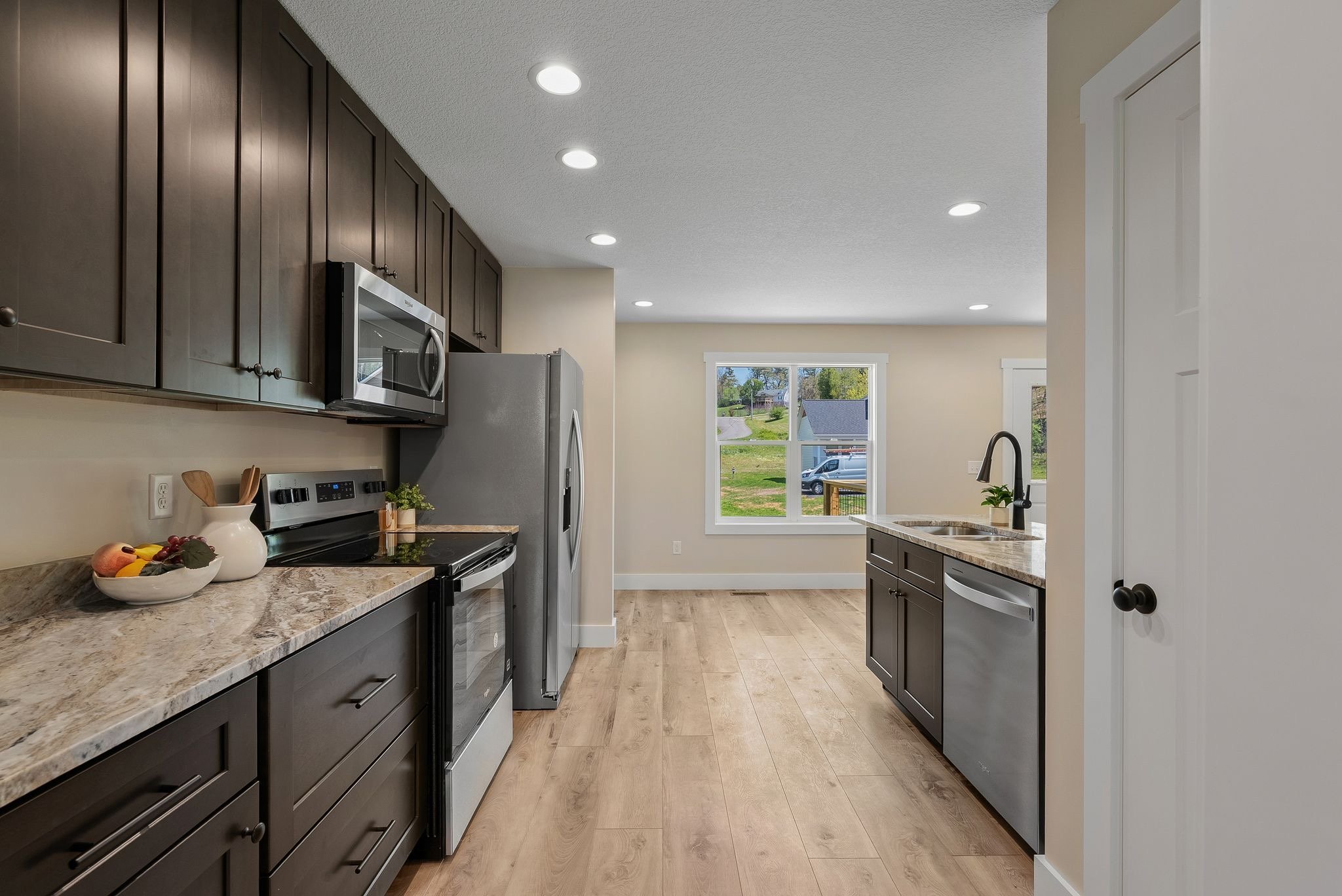 Kitchen with dark cabinets, granite countertops, stainless steel appliances, and a large window overlooking a grassy yard.